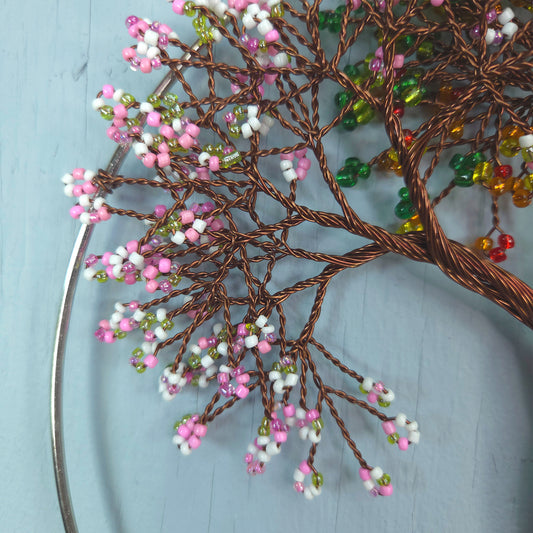 Decorative wall art with wire tree branches and colorful beads on a light blue background