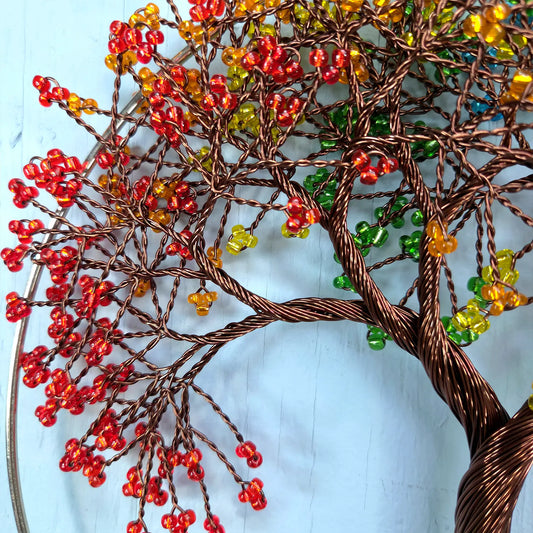 Decorative tree sculpture with red, orange, and green beads on a light blue background