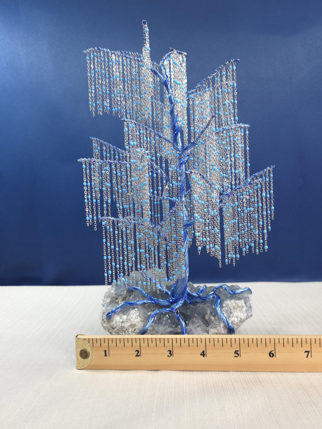 Decorative blue and silver tree-like sculpture on a white surface with a ruler for scale against a blue background