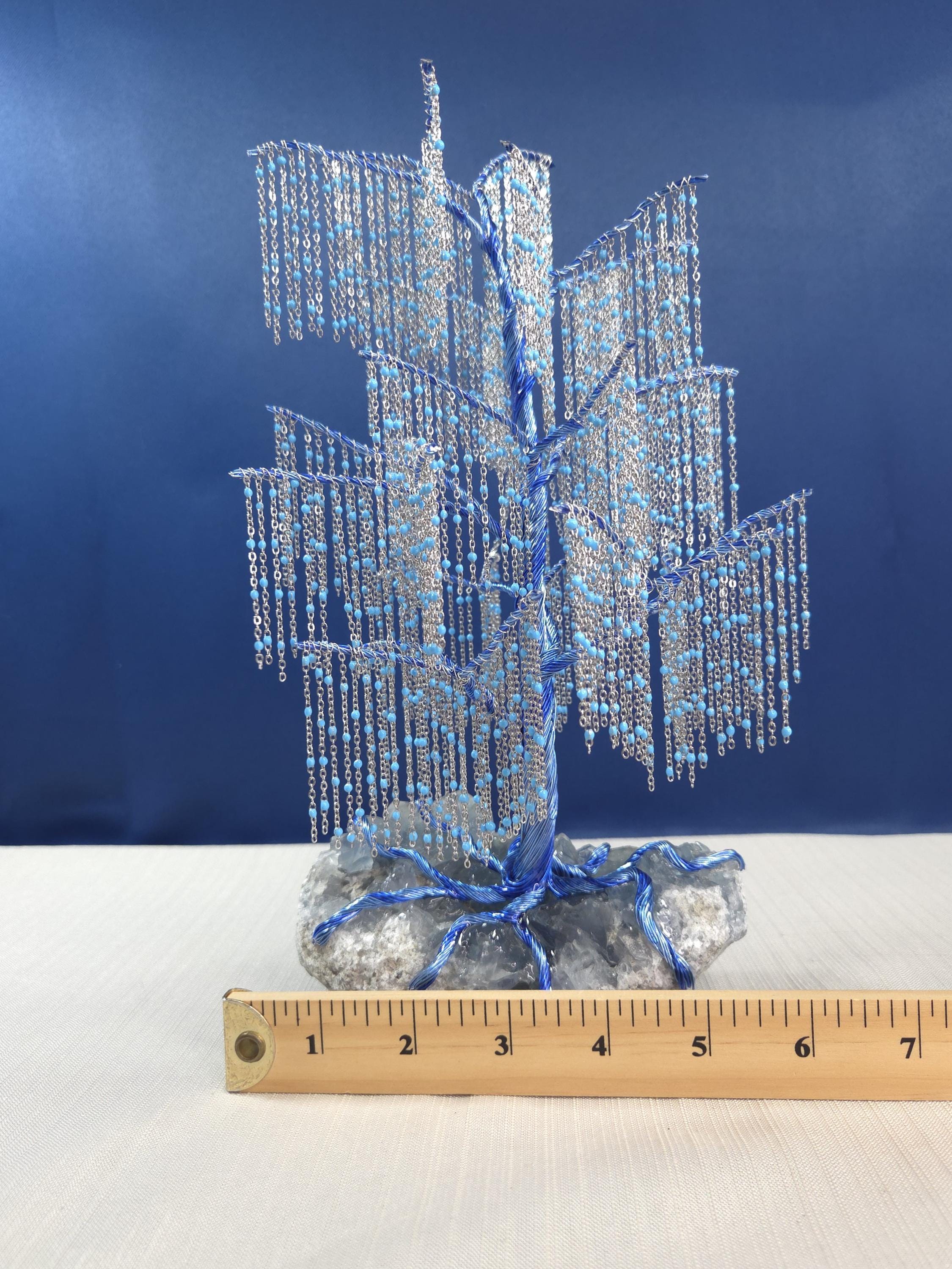 Decorative blue and silver tree-like sculpture on a white surface with a ruler for scale against a blue background