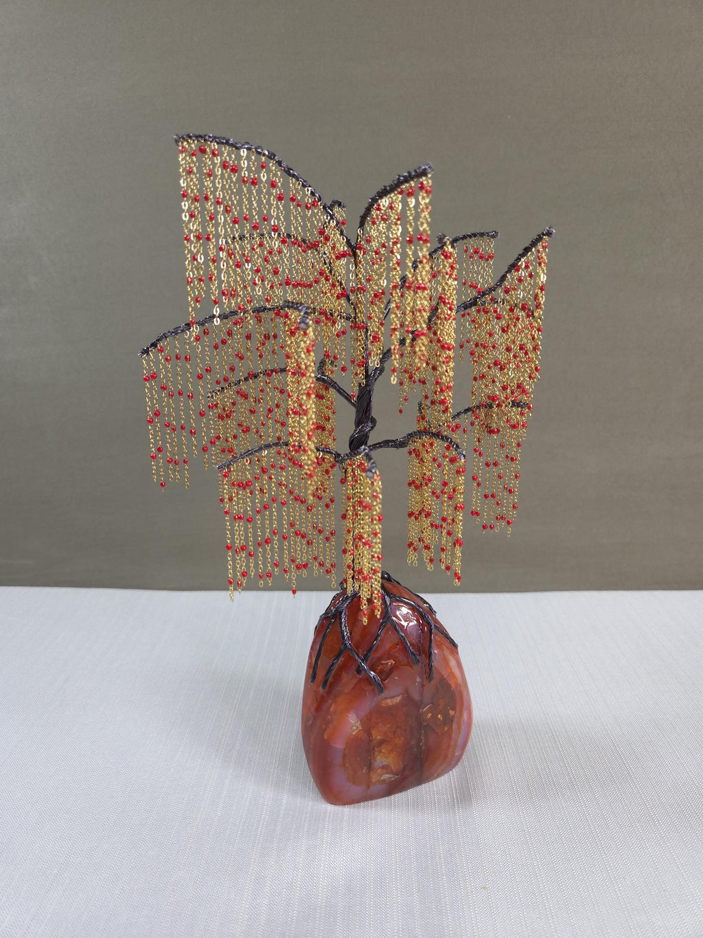 Decorative beaded tree sculpture on a stone base against a plain background