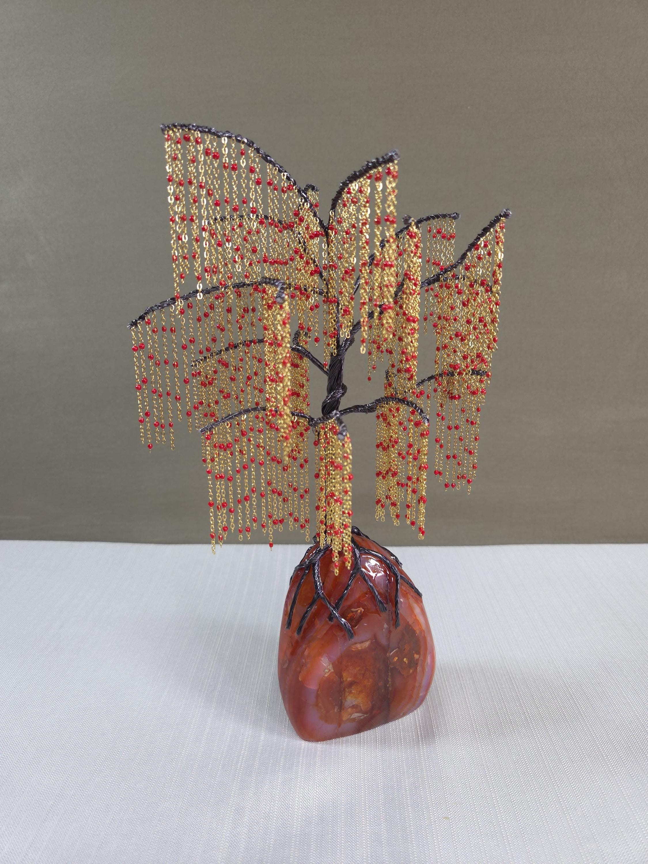 Decorative beaded tree sculpture on a stone base against a plain background