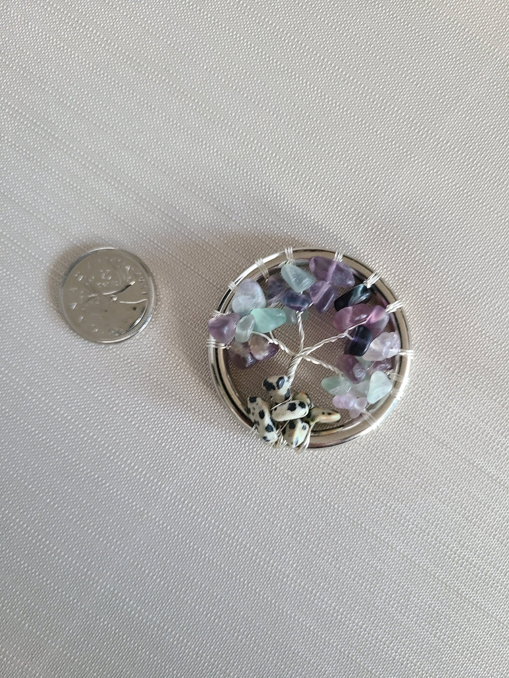 Small round decorative item with colorful stones and a coin for scale on a light gray background