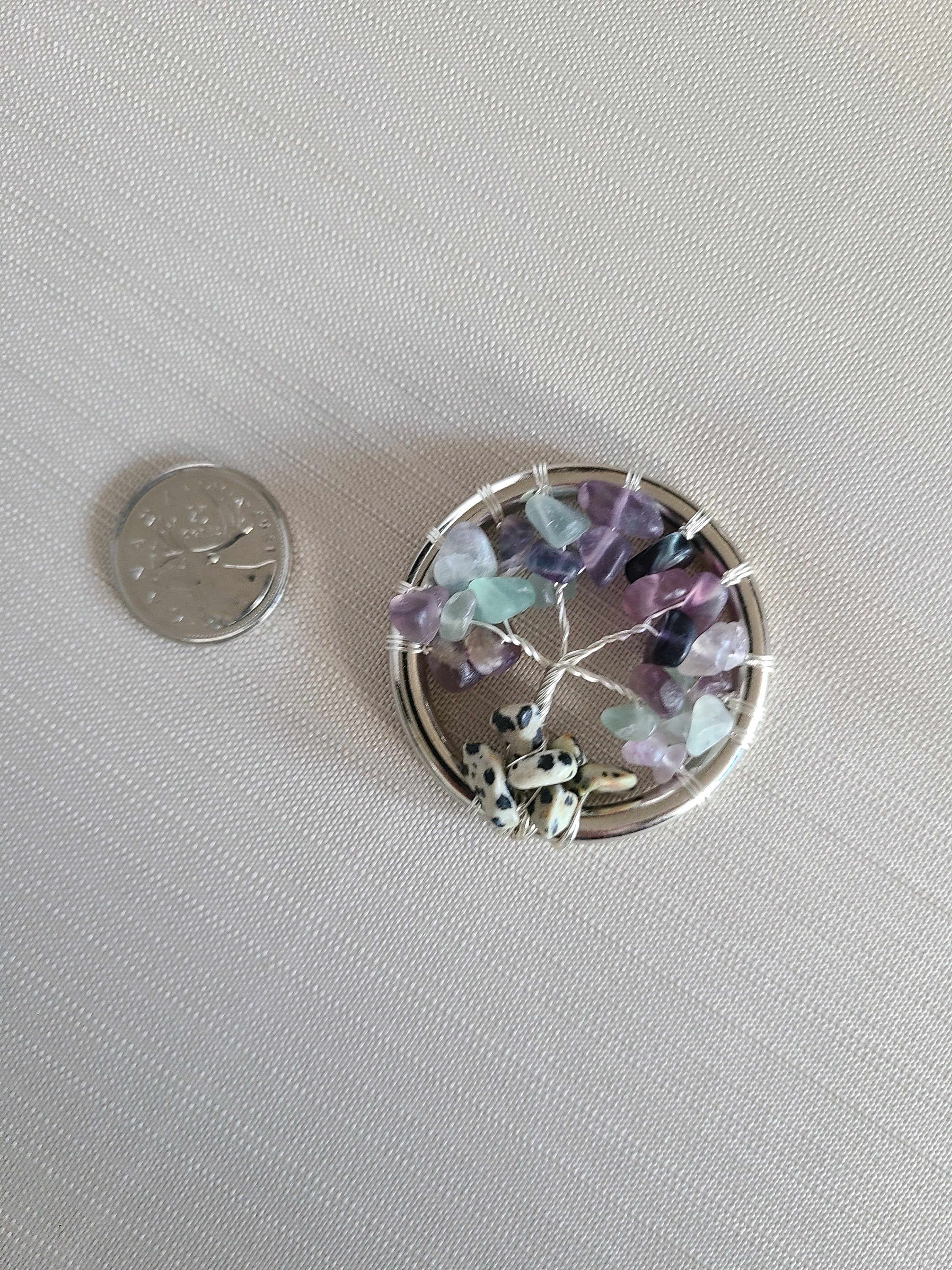 Small round decorative item with colorful stones and a coin for scale on a light gray background