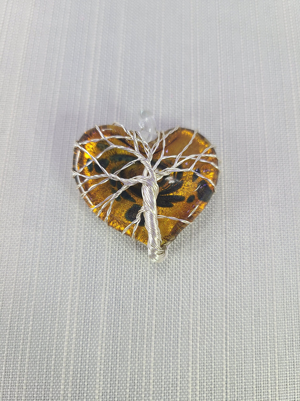 Heart-shaped amber stone with silver tree of life design on a light gray background