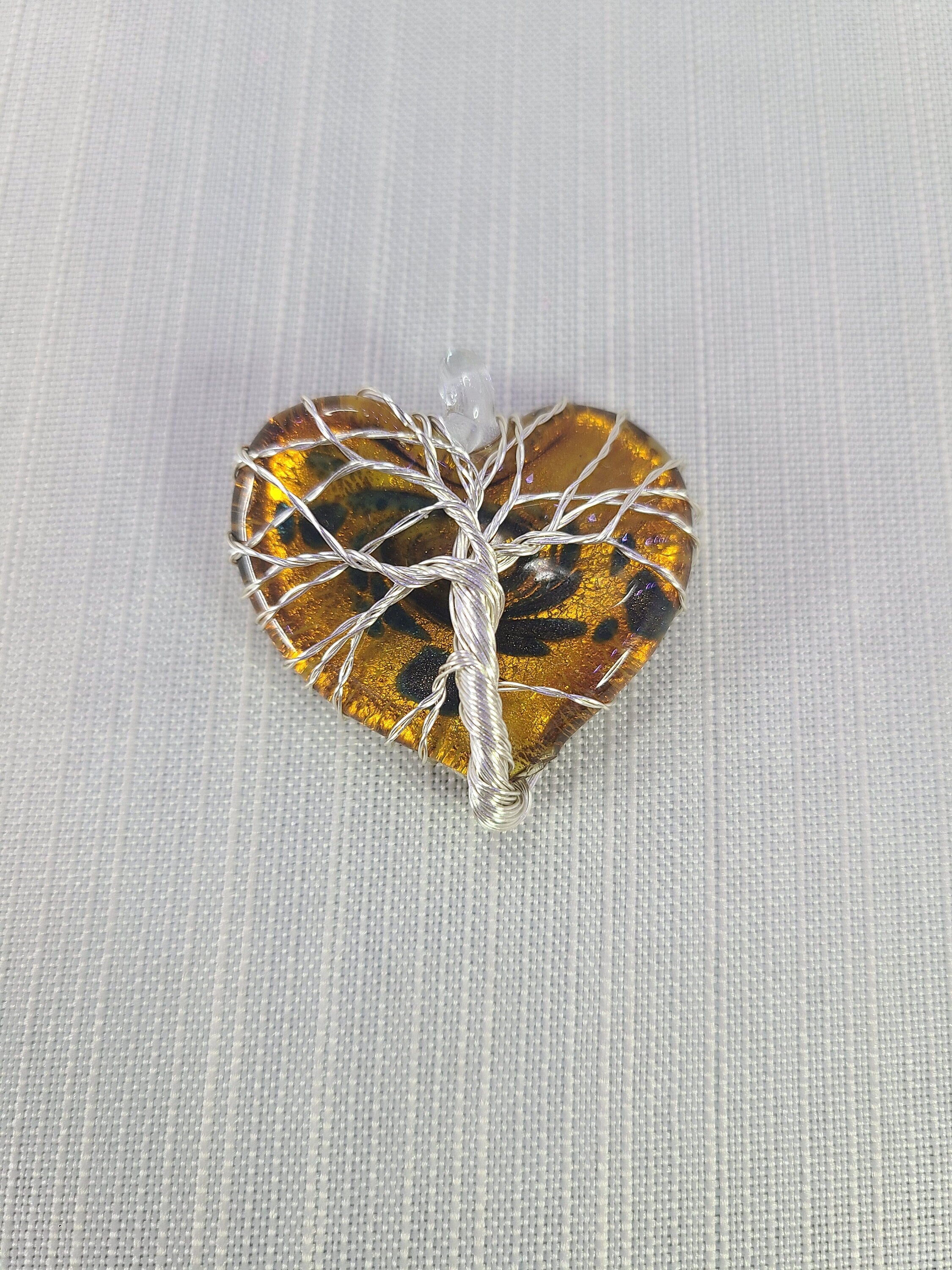 Heart-shaped amber stone with silver tree of life design on a light gray background