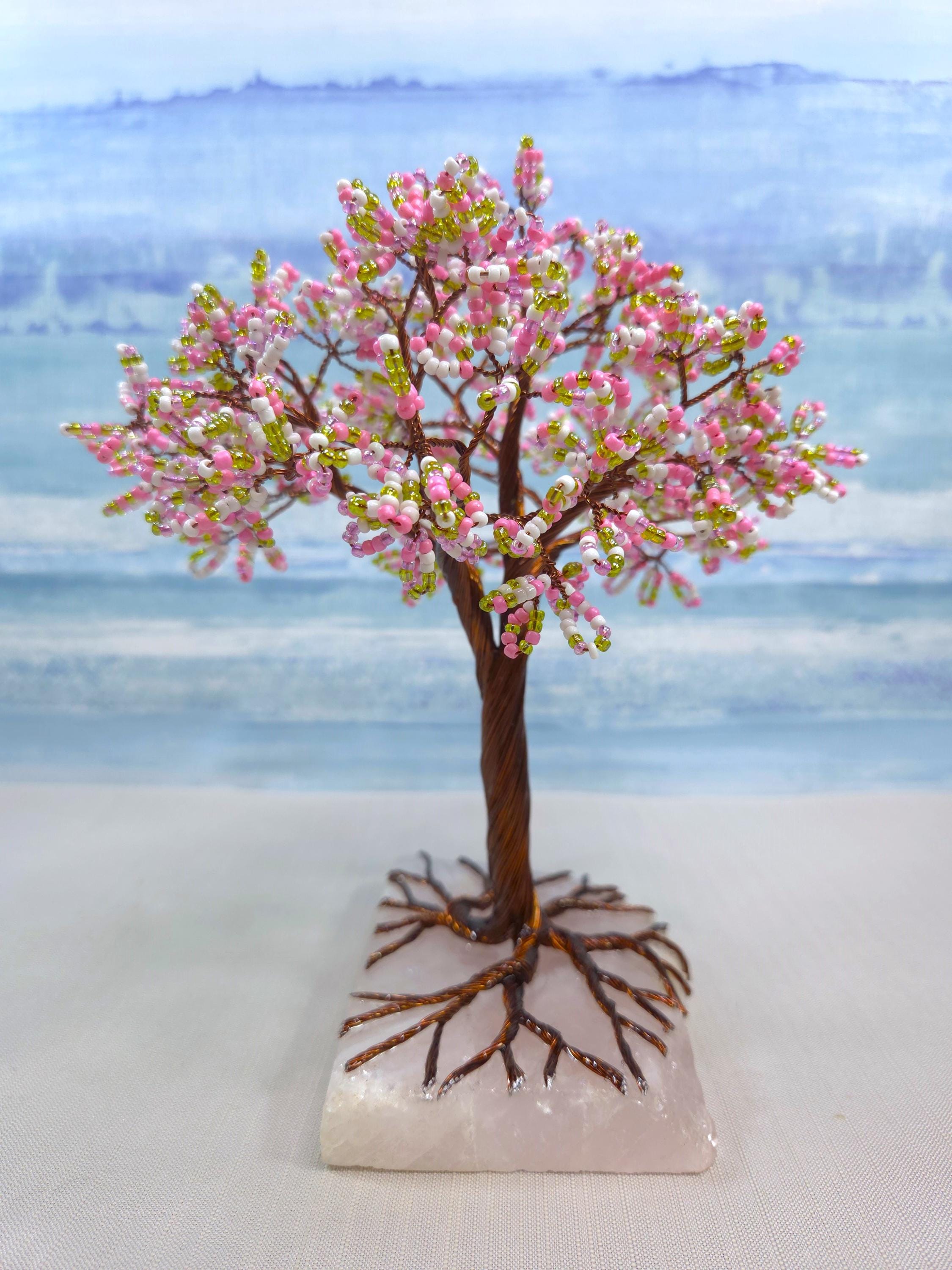 Decorative tree with pink blossoms on a white base against a blue watercolor background