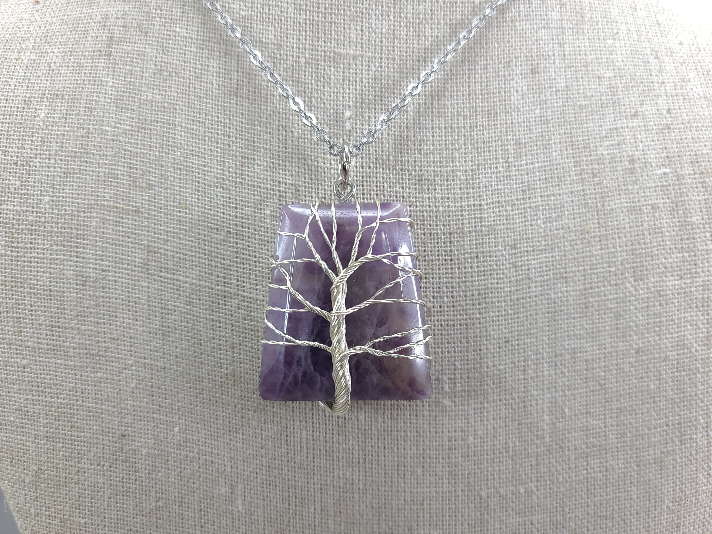 Necklace with a purple pendant featuring a silver tree design on a gray background