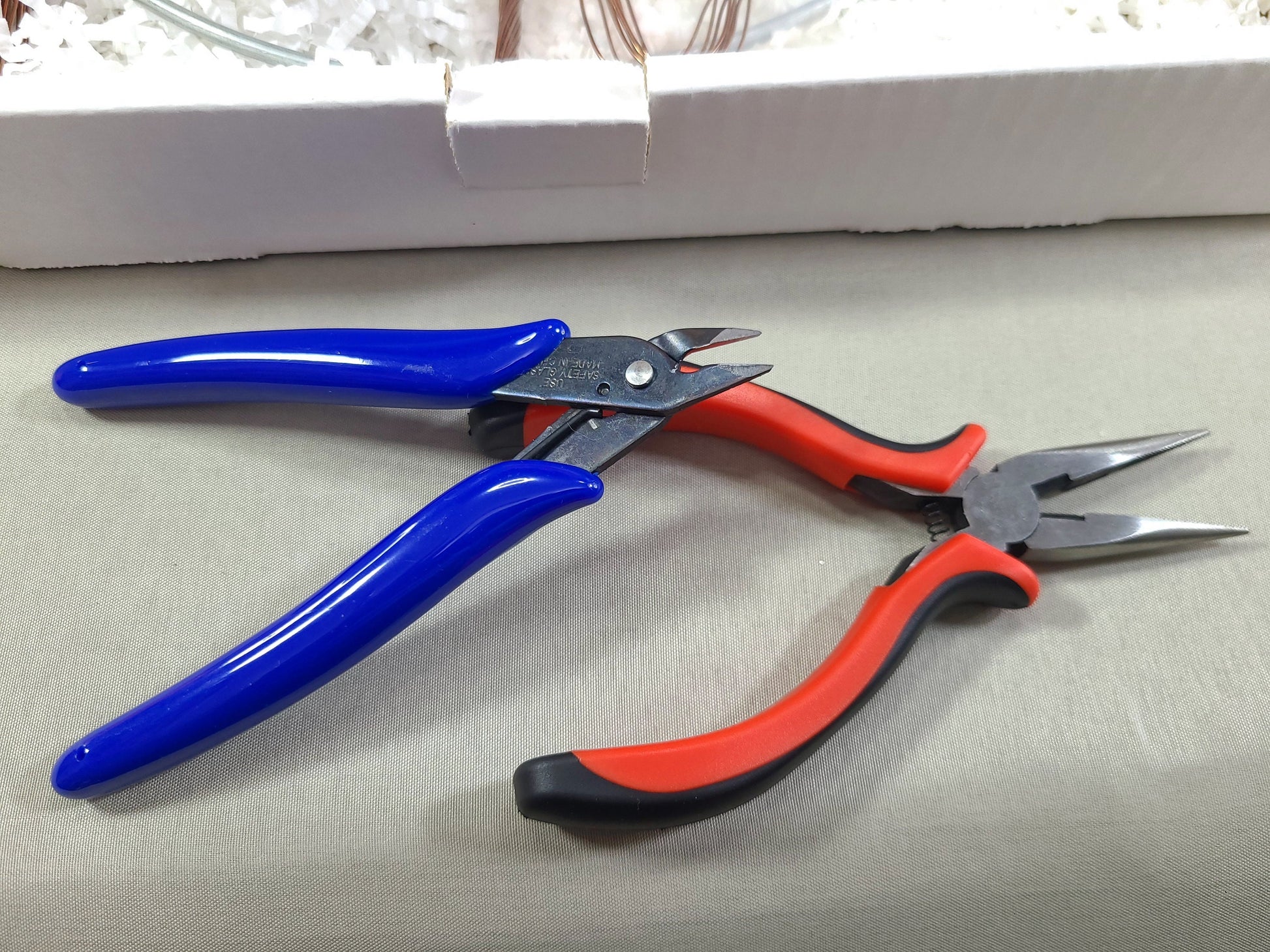 Pair of blue-handled pliers and red-handled wire cutters on a light gray surface.
