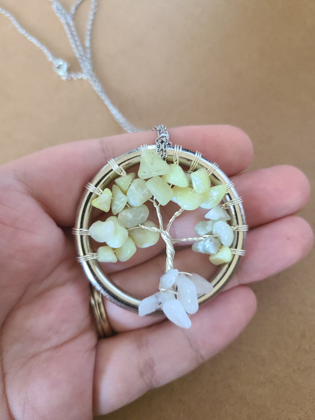 Hand holding a tree-shaped pendant with green stones and a beige background