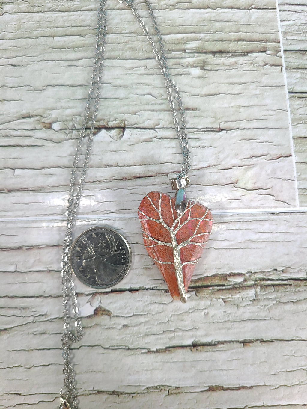 Heart-shaped pendant on a chain next to a quarter for scale, on a wooden surface