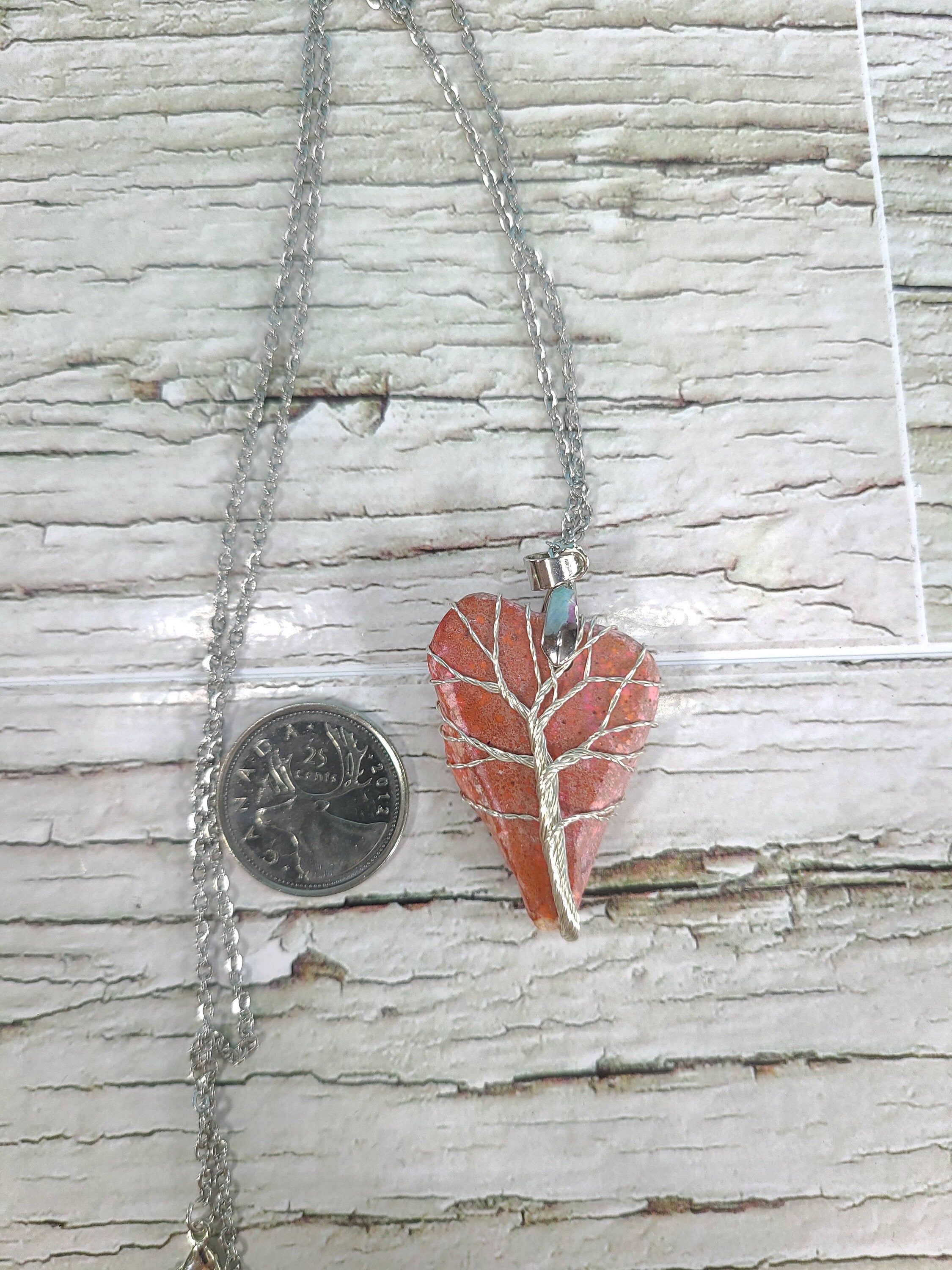 Heart-shaped pendant on a chain next to a quarter for scale, on a wooden surface