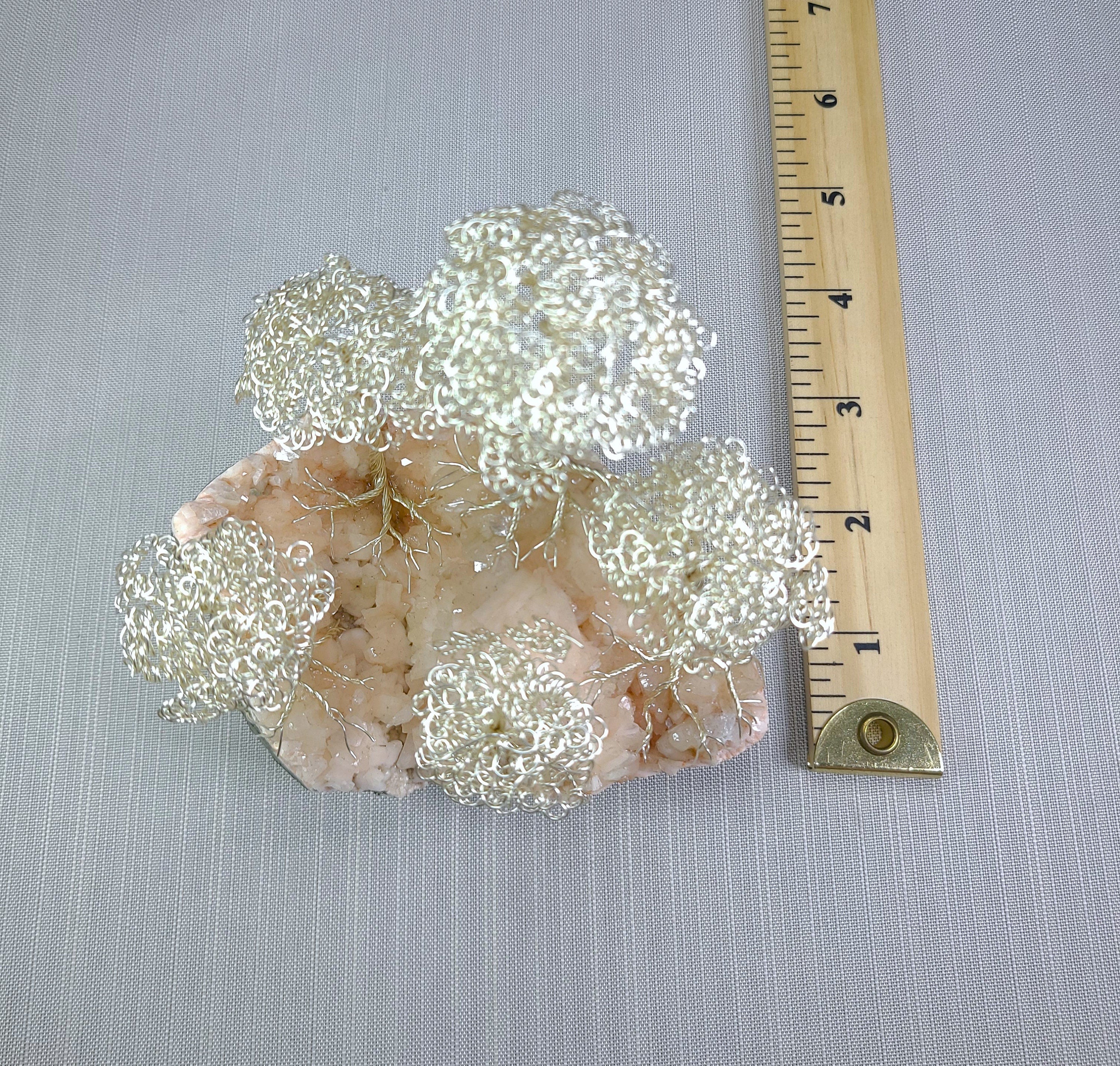 Decorative wire mesh on a stone base with a ruler for scale on a gray background