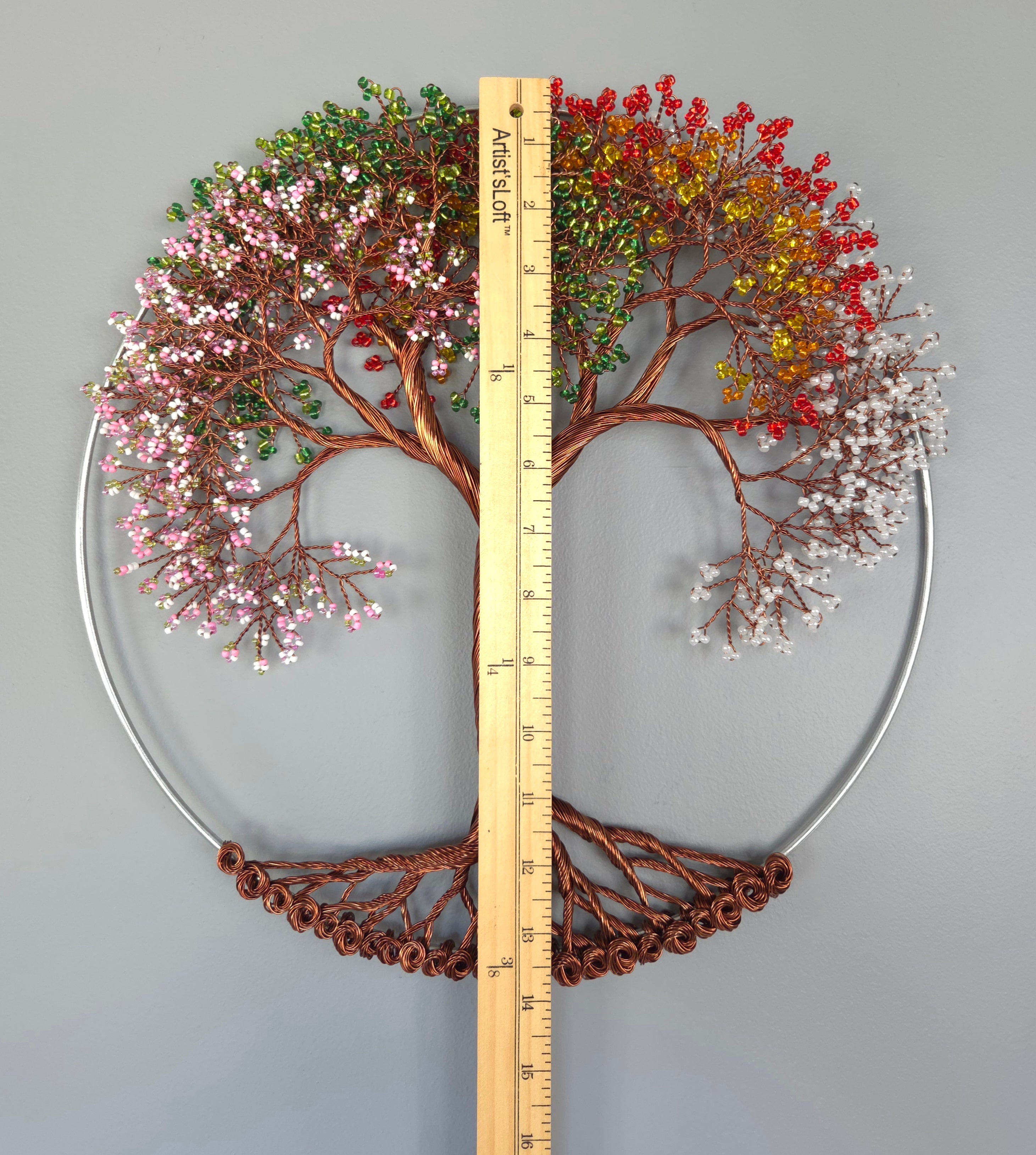 Decorative wall art of a tree with colorful leaves and a ruler for scale on a gray background