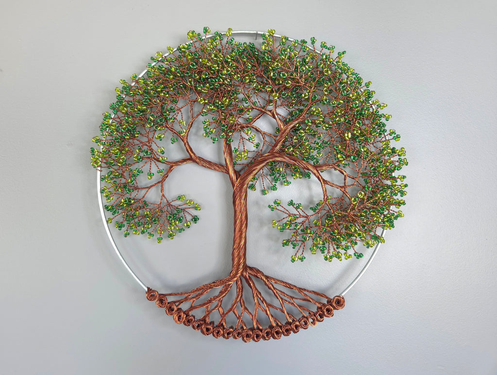 Decorative wall art of a tree with copper branches and green leaves on a light gray background