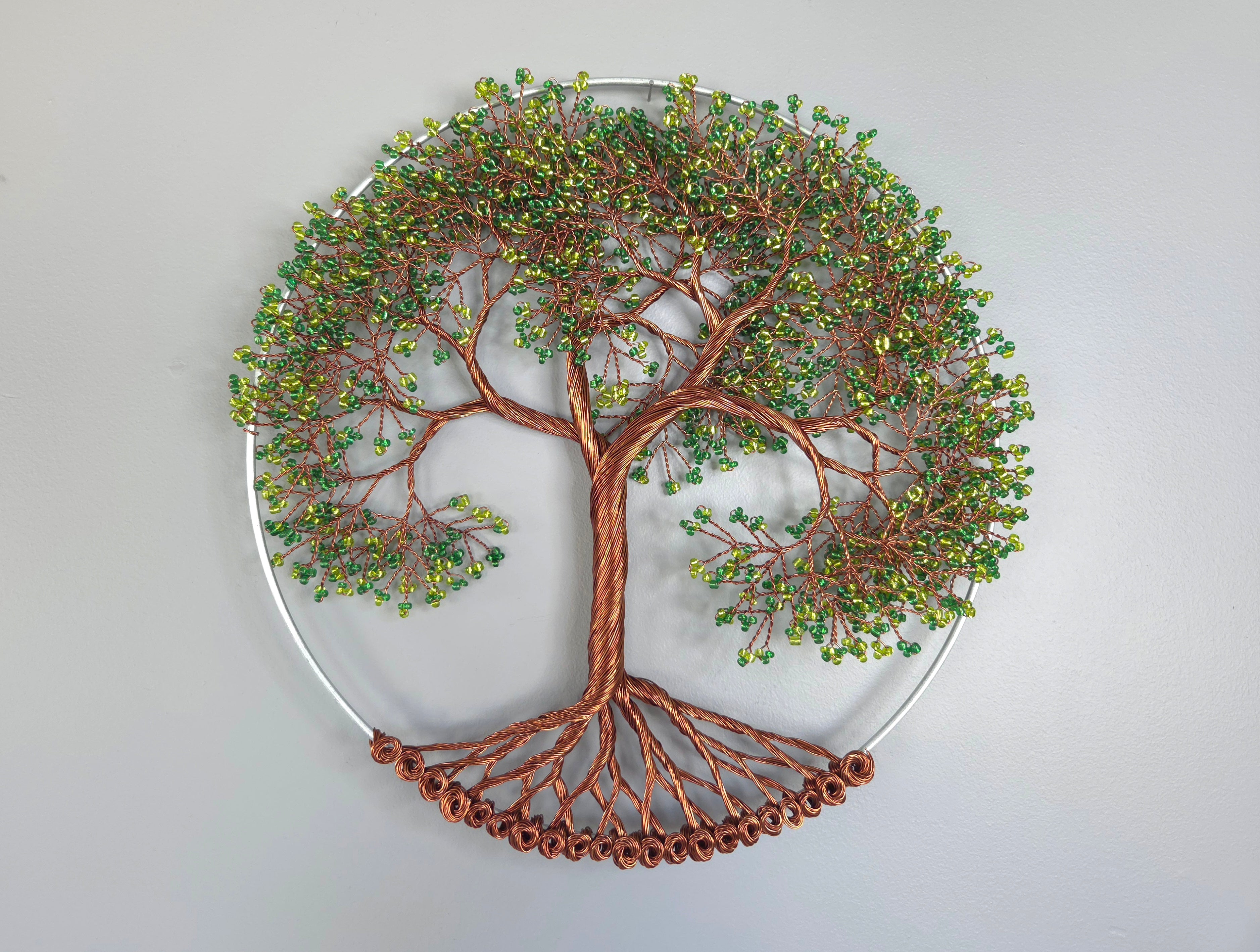 Decorative wall art of a tree with copper branches and green leaves on a light gray background