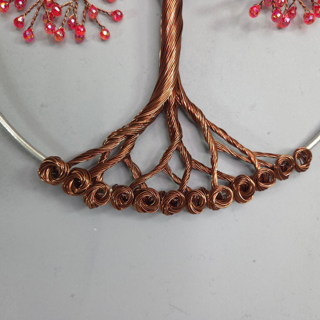 Copper wire tree sculpture with pink beads on a light gray background