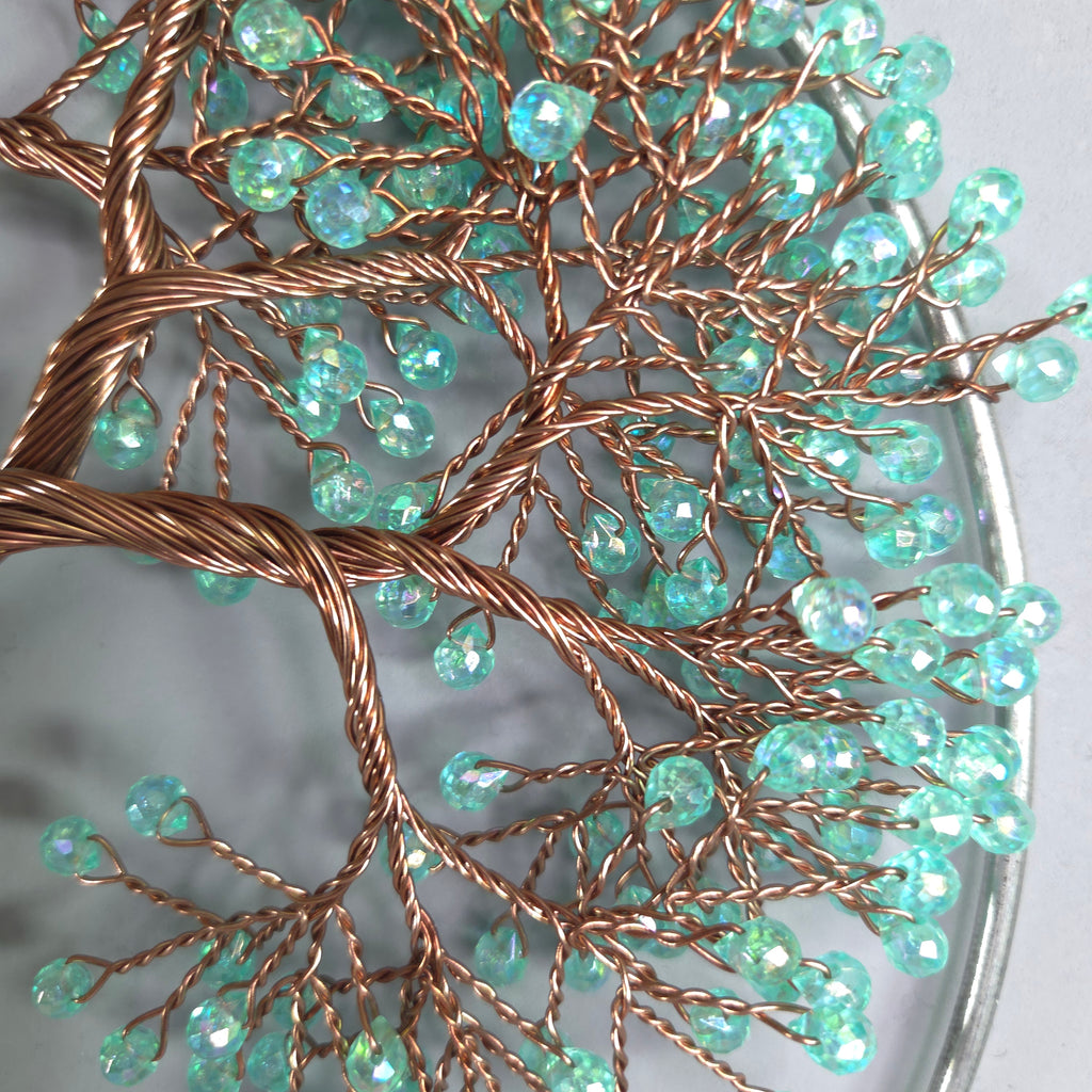 Decorative tree sculpture with turquoise beads on a reflective surface