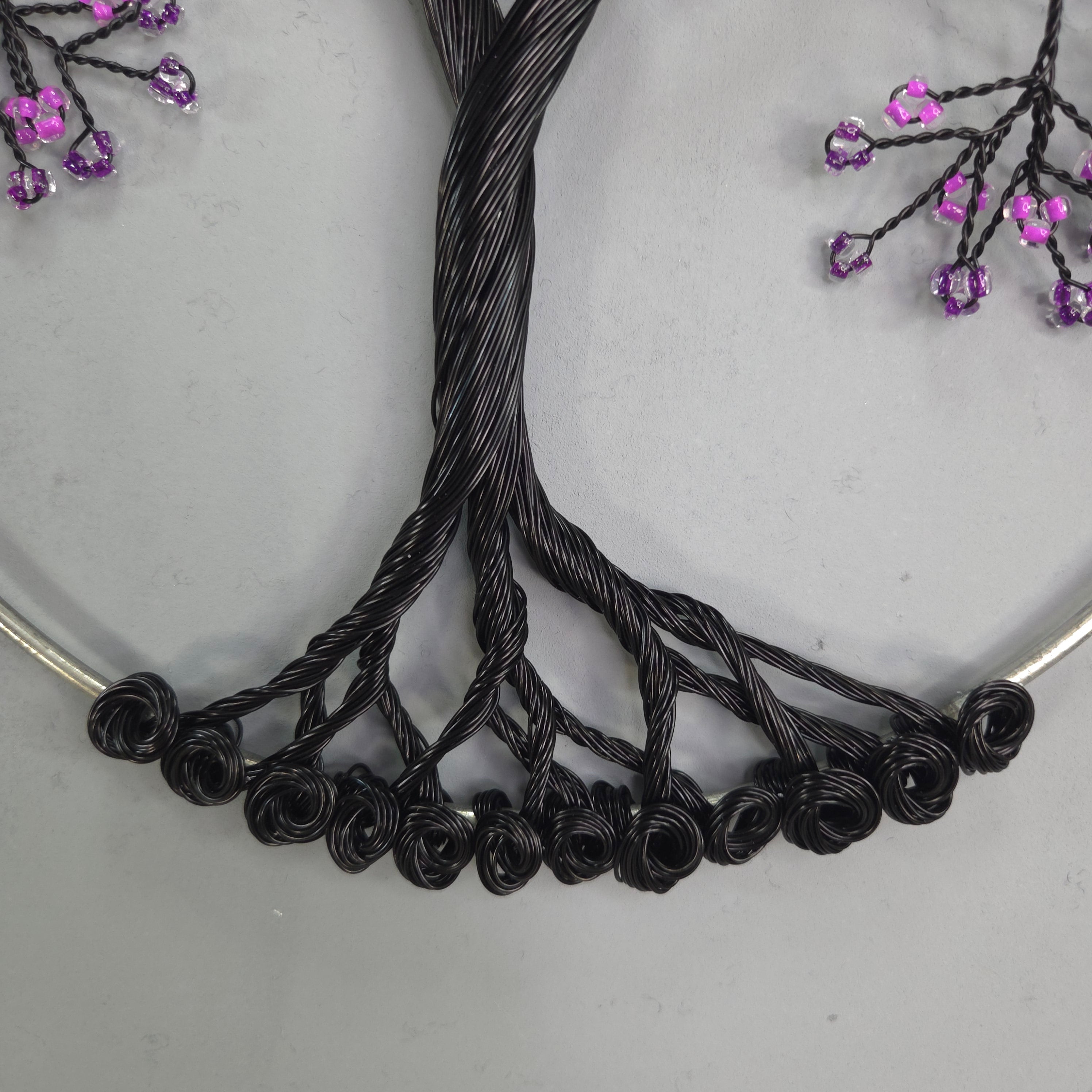 Black wire sculpture on a white surface with purple flowers.