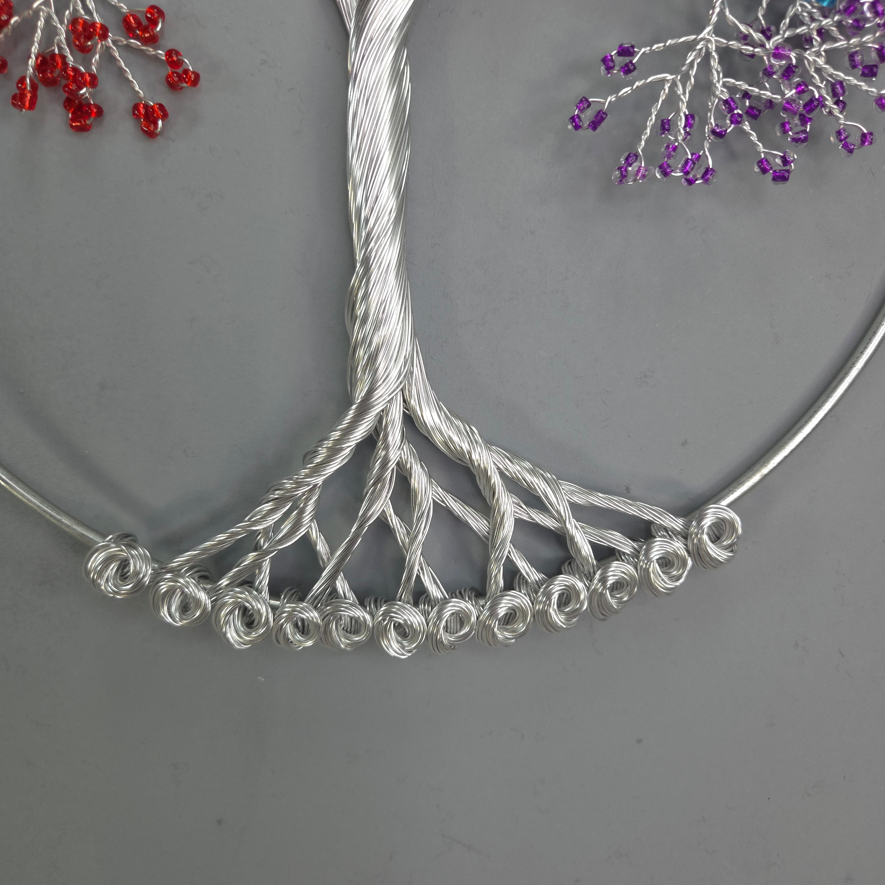 Silver wire tree branch with purple and red bead decorations on a gray background