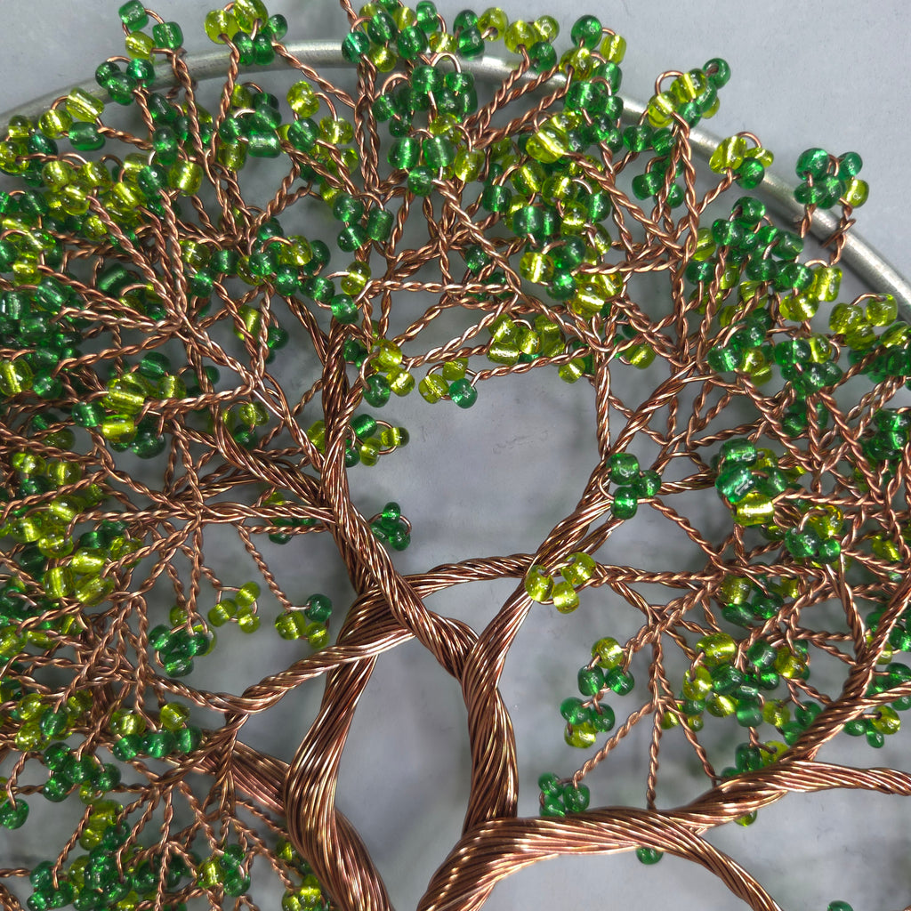 Decorative wall art with green beads and copper wire on a white background