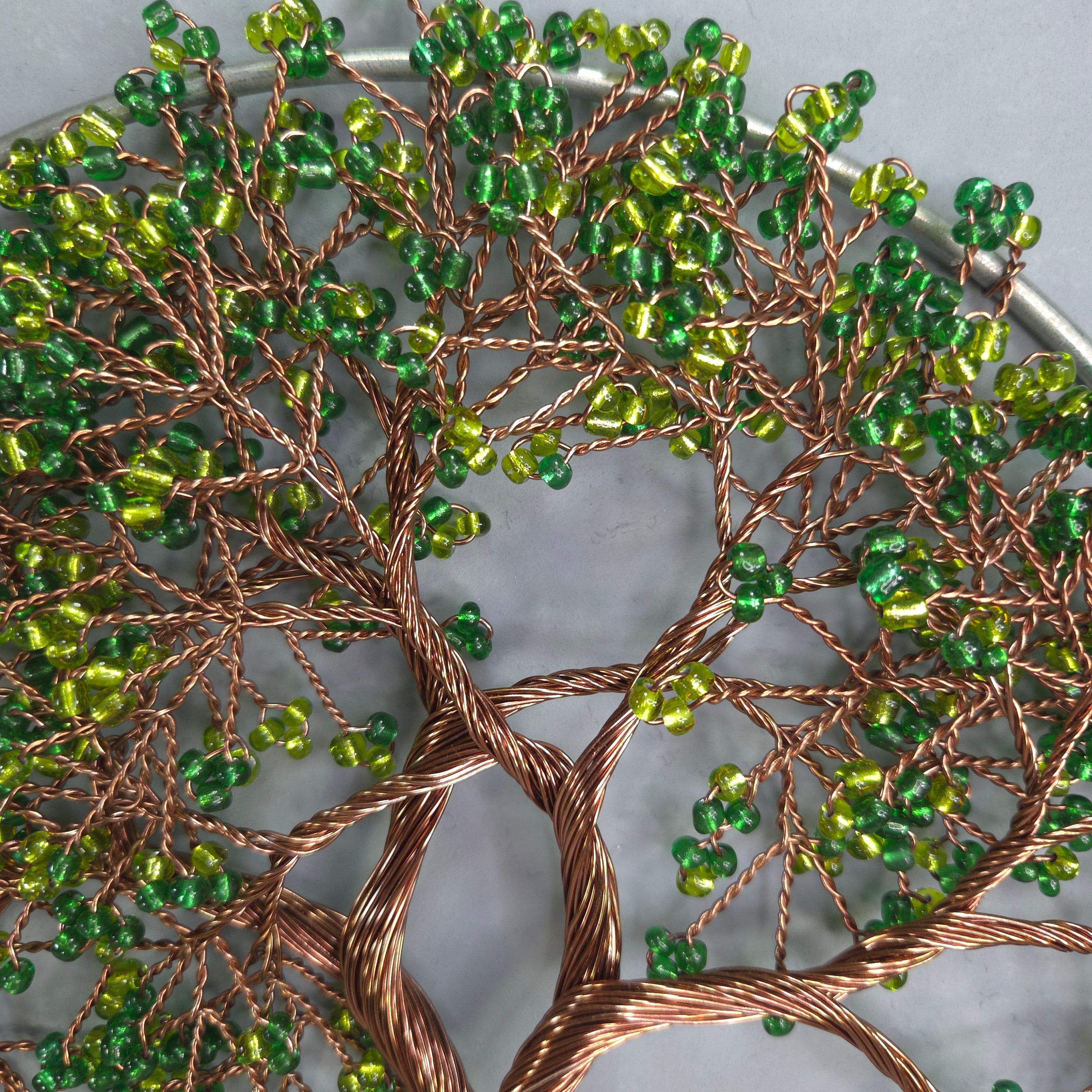 Decorative wall art with green beads and copper wire on a white background