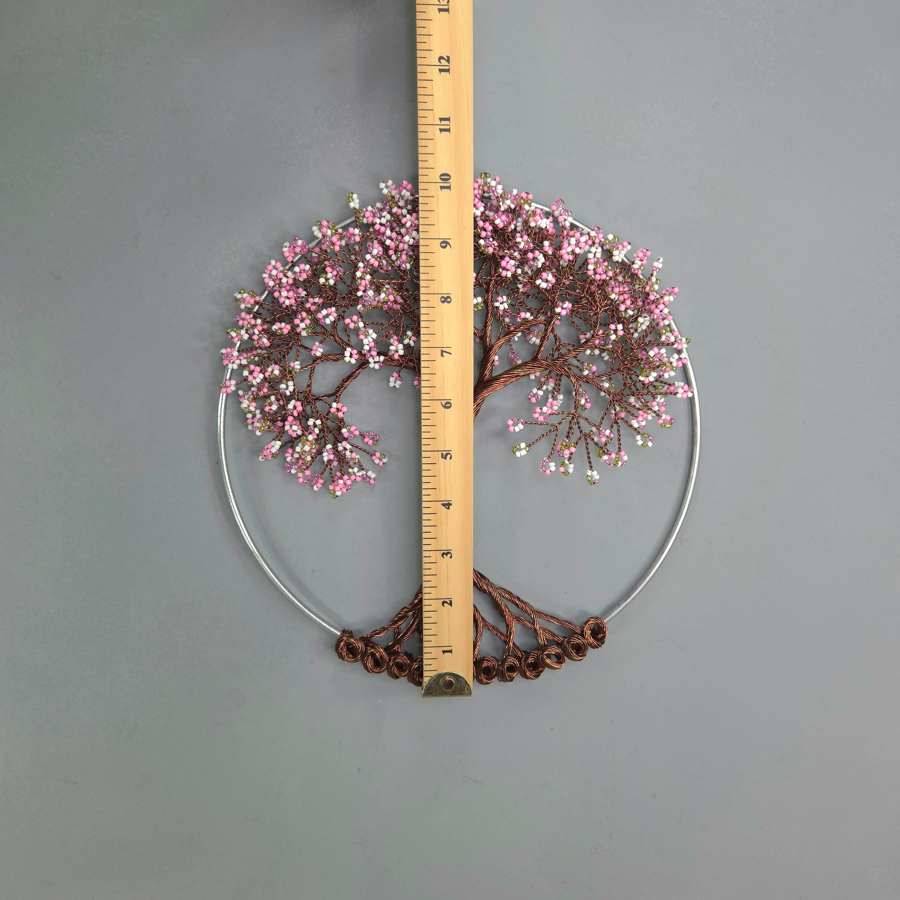 Decorative wall piece with pink blossoms and a ruler for scale on a gray background