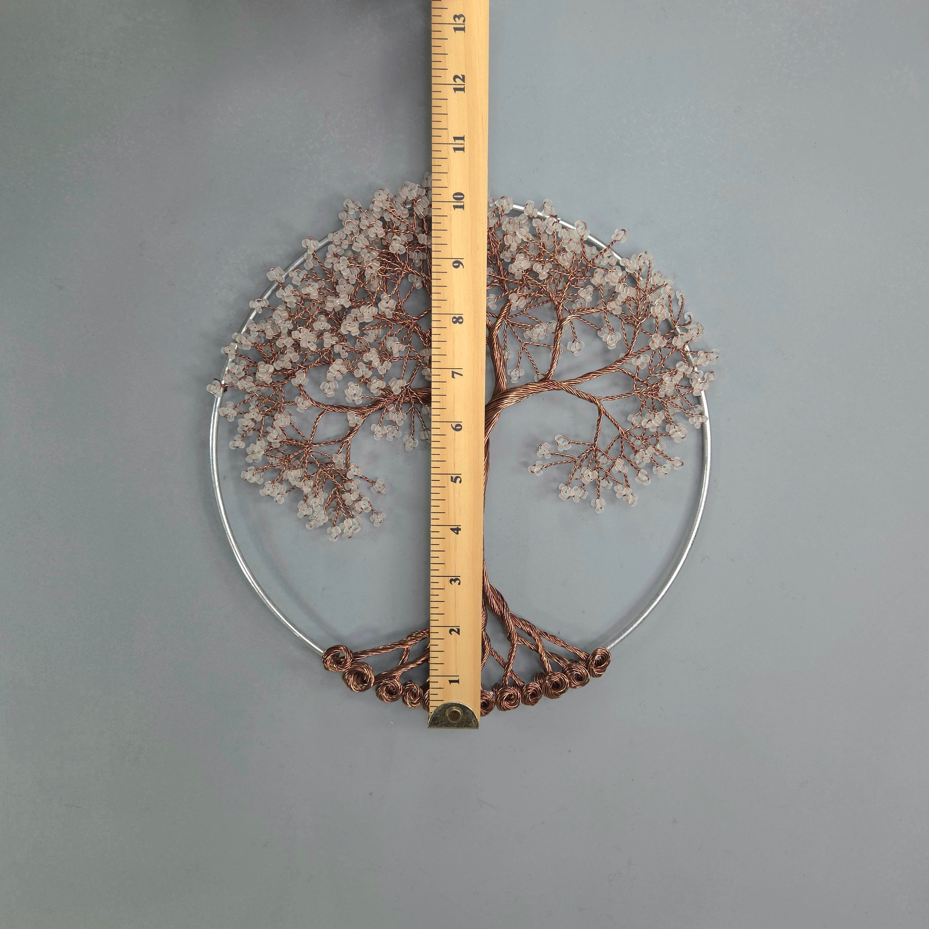 Decorative wreath with branches and flowers, measured against a ruler on a gray background