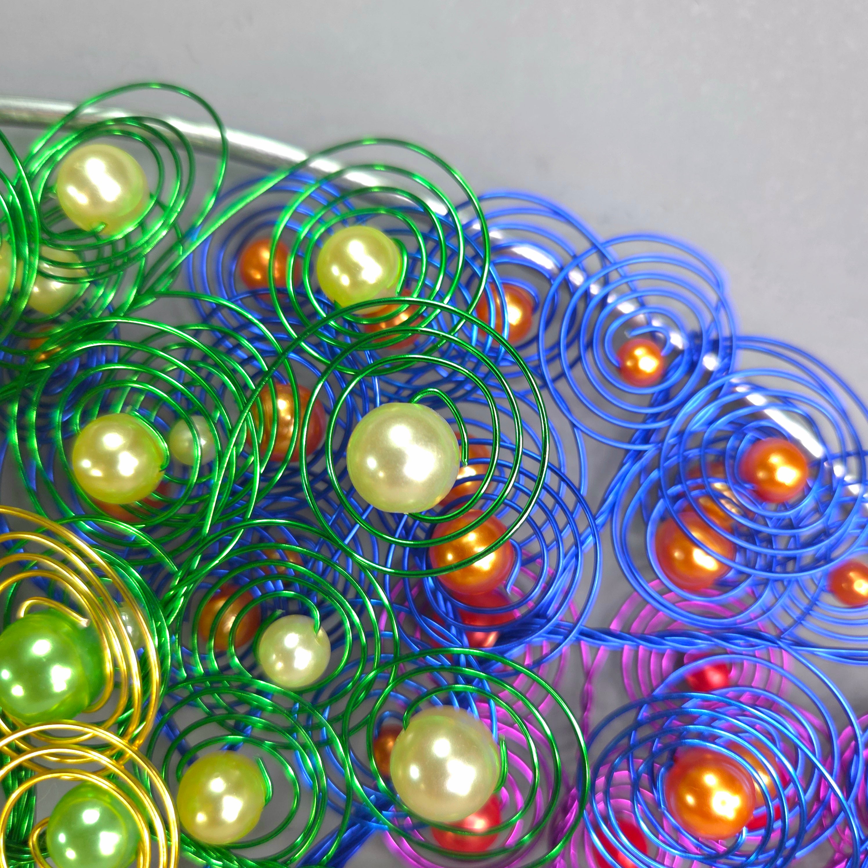 Colorful metal coils with embedded pearls on a gray background