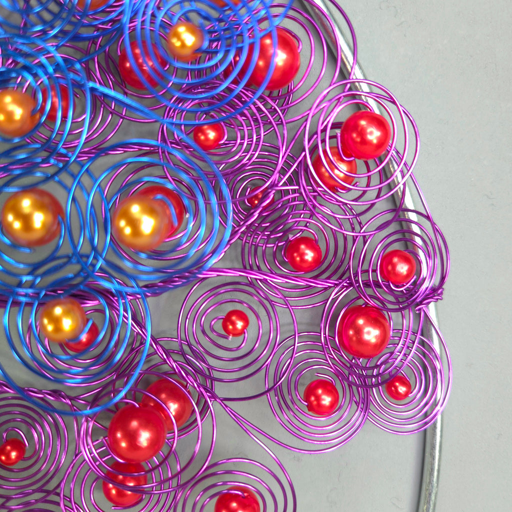 Decorative wreath with purple and blue wire swirls and red balls on a plain background