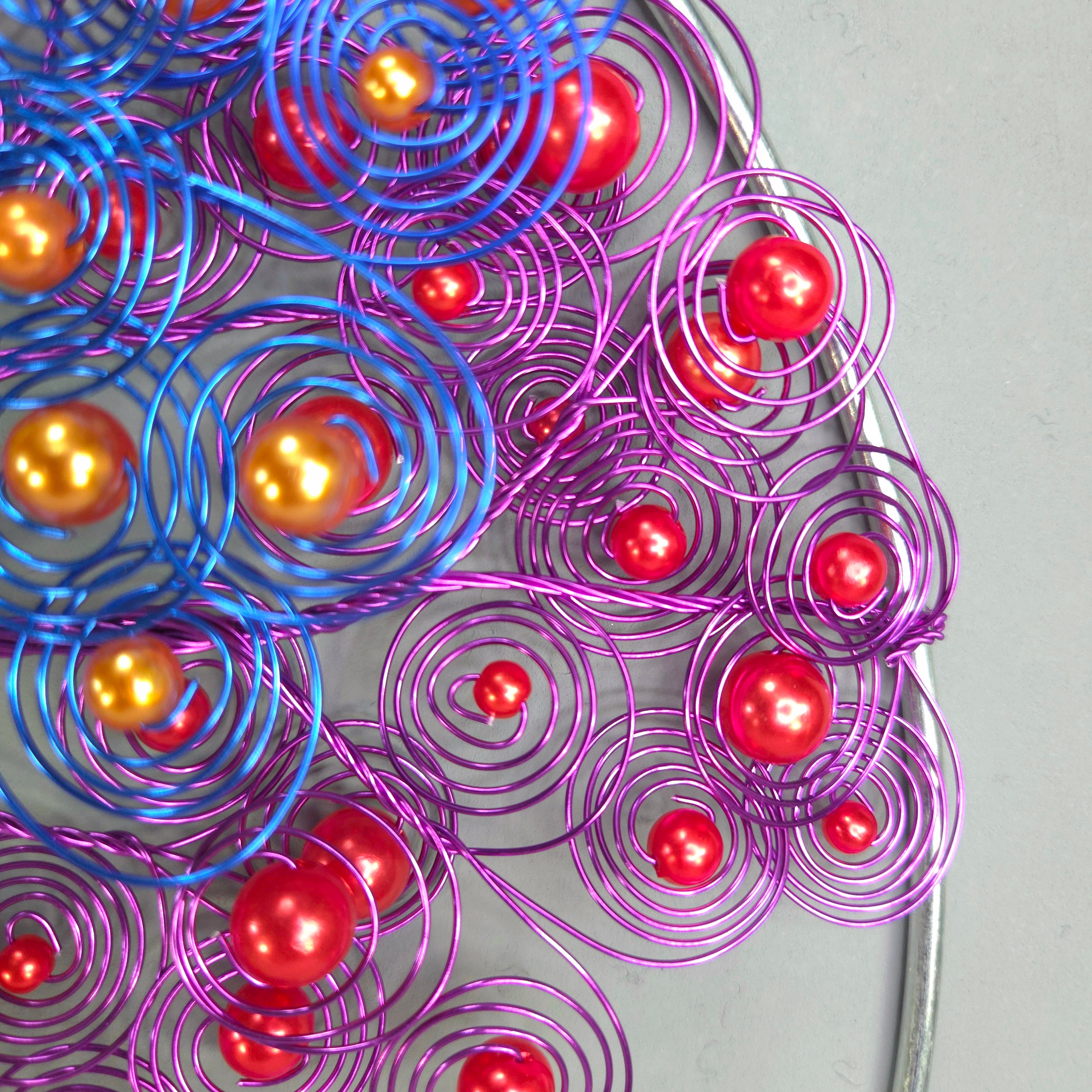 Decorative wreath with purple and blue wire swirls and red balls on a plain background