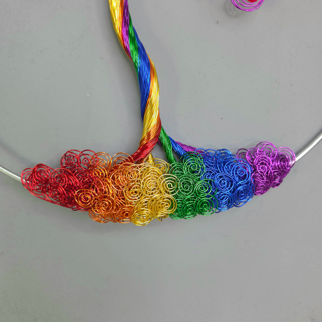 Colorful wire loops arranged in a rainbow pattern on a gray surface.