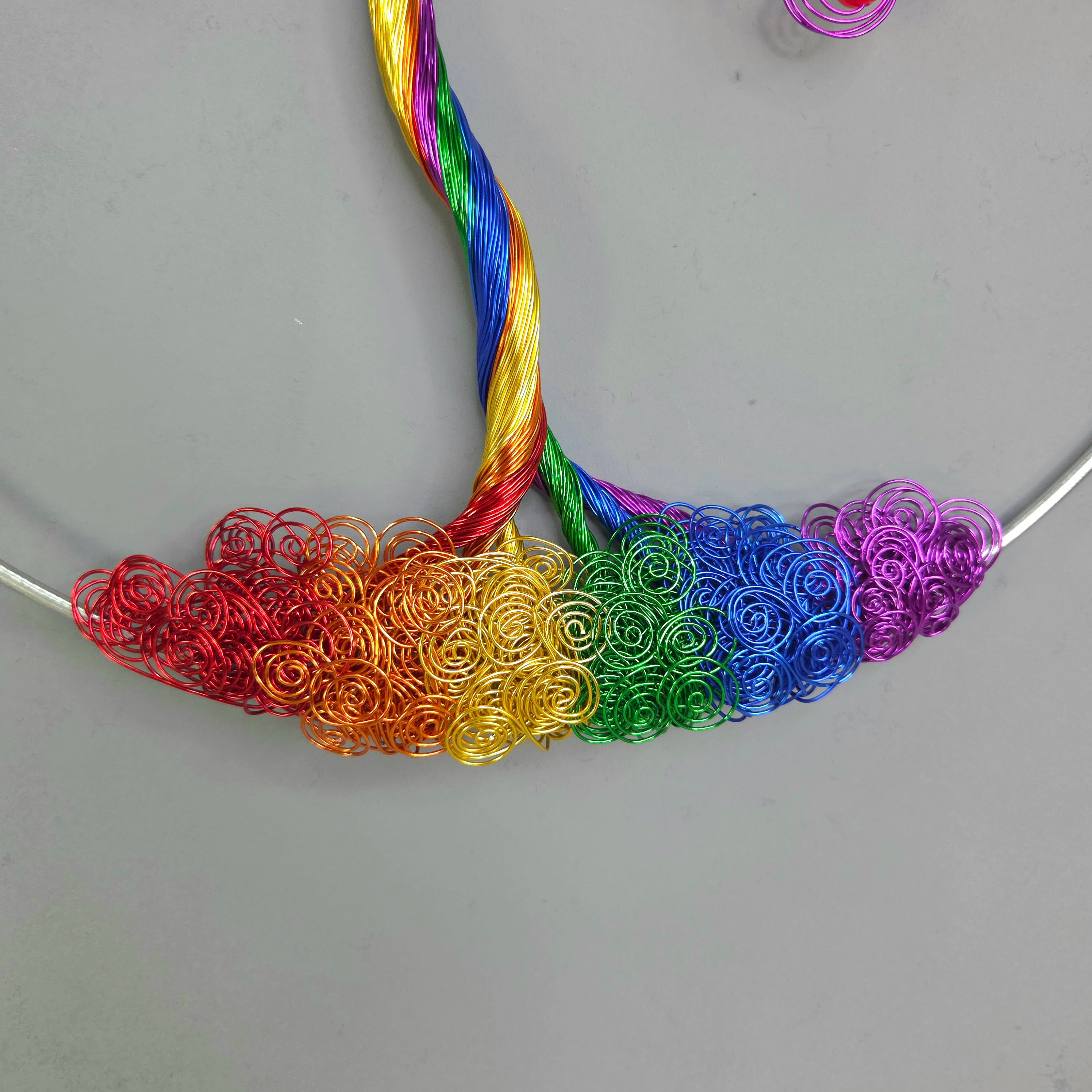 Colorful wire loops arranged in a rainbow pattern on a gray surface.