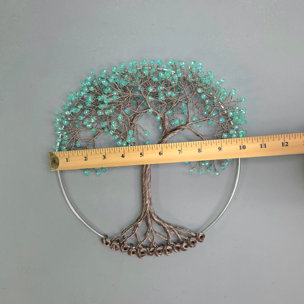 Decorative wall art in the shape of a tree with turquoise beads and a measuring tape for scale on a gray background.