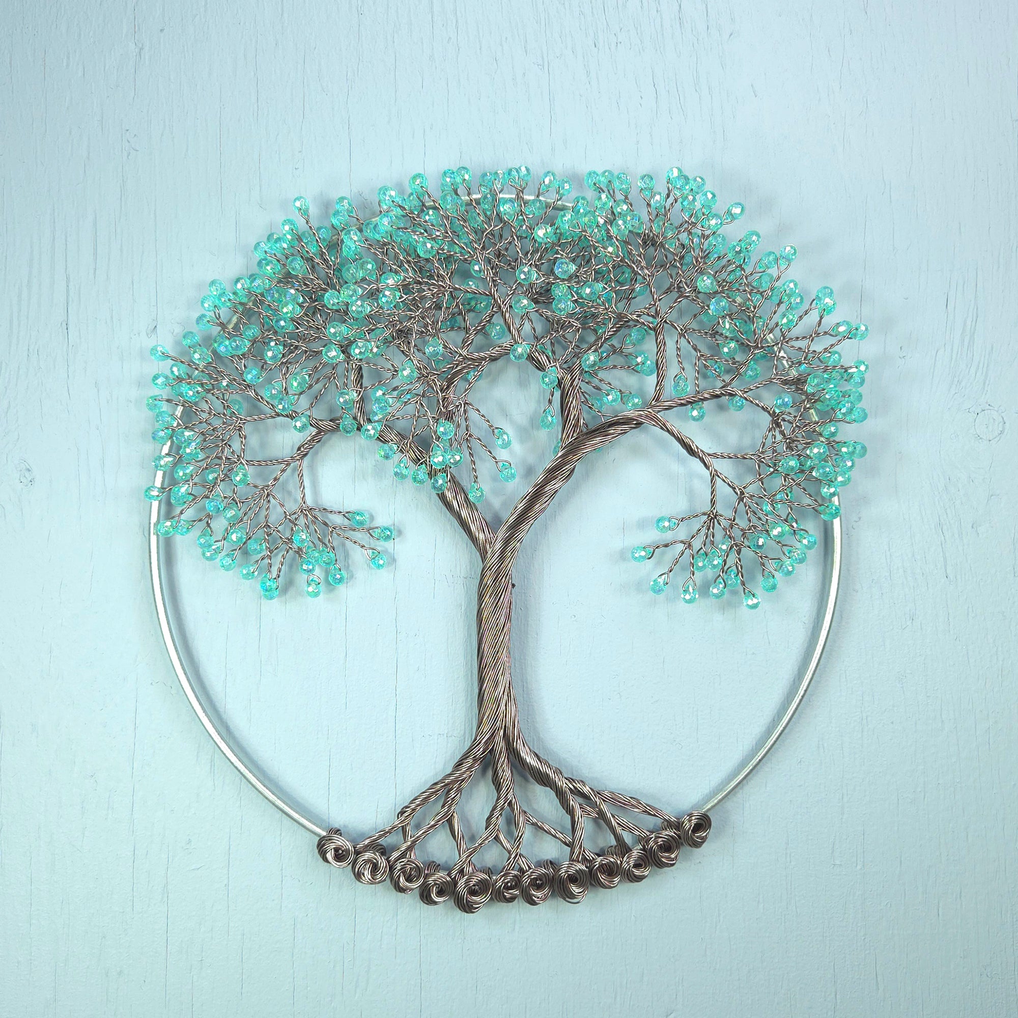 Decorative wall art of a tree with turquoise beads on a light blue background