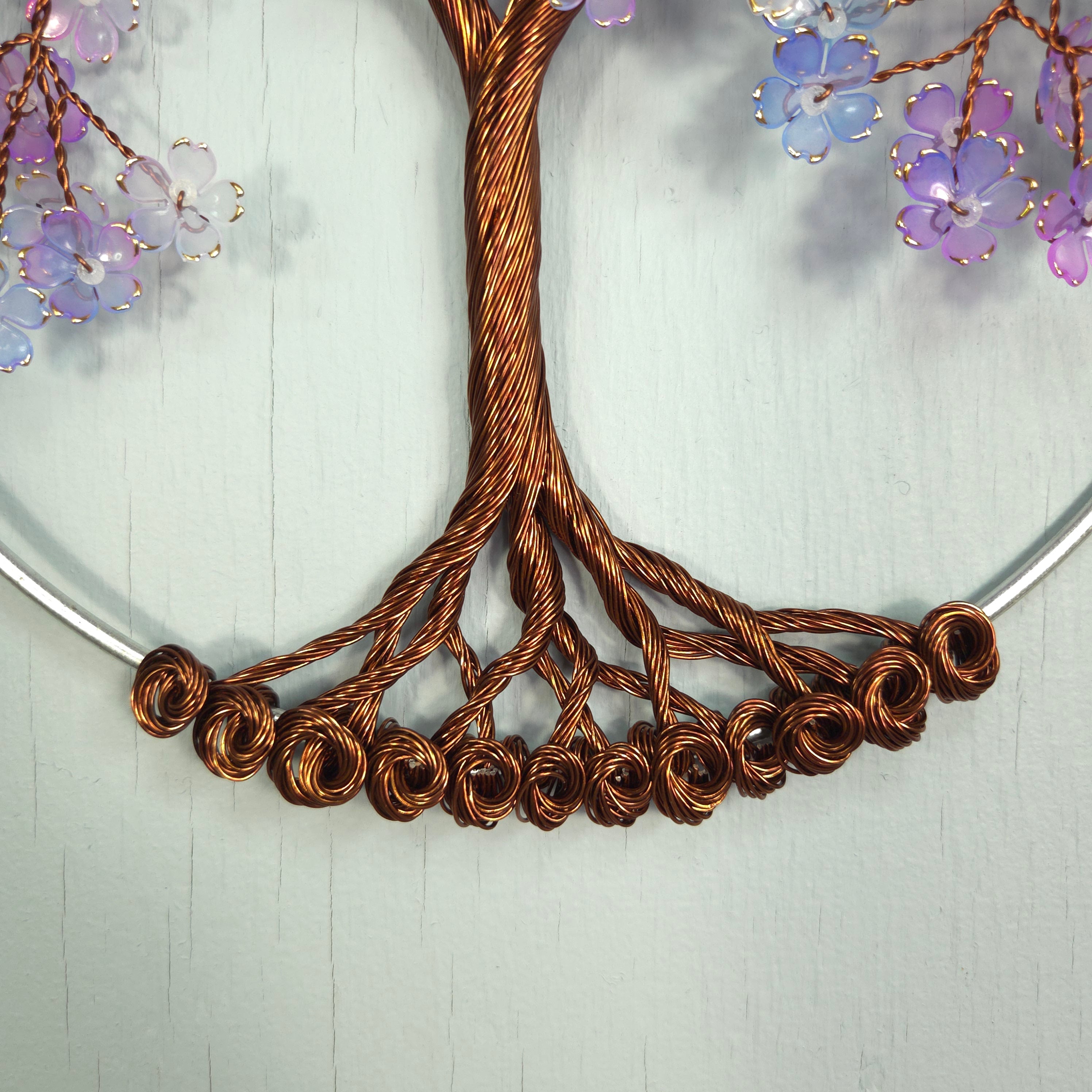 Close-up of a decorative wreath with twisted copper wire and purple flowers on a light wooden background.