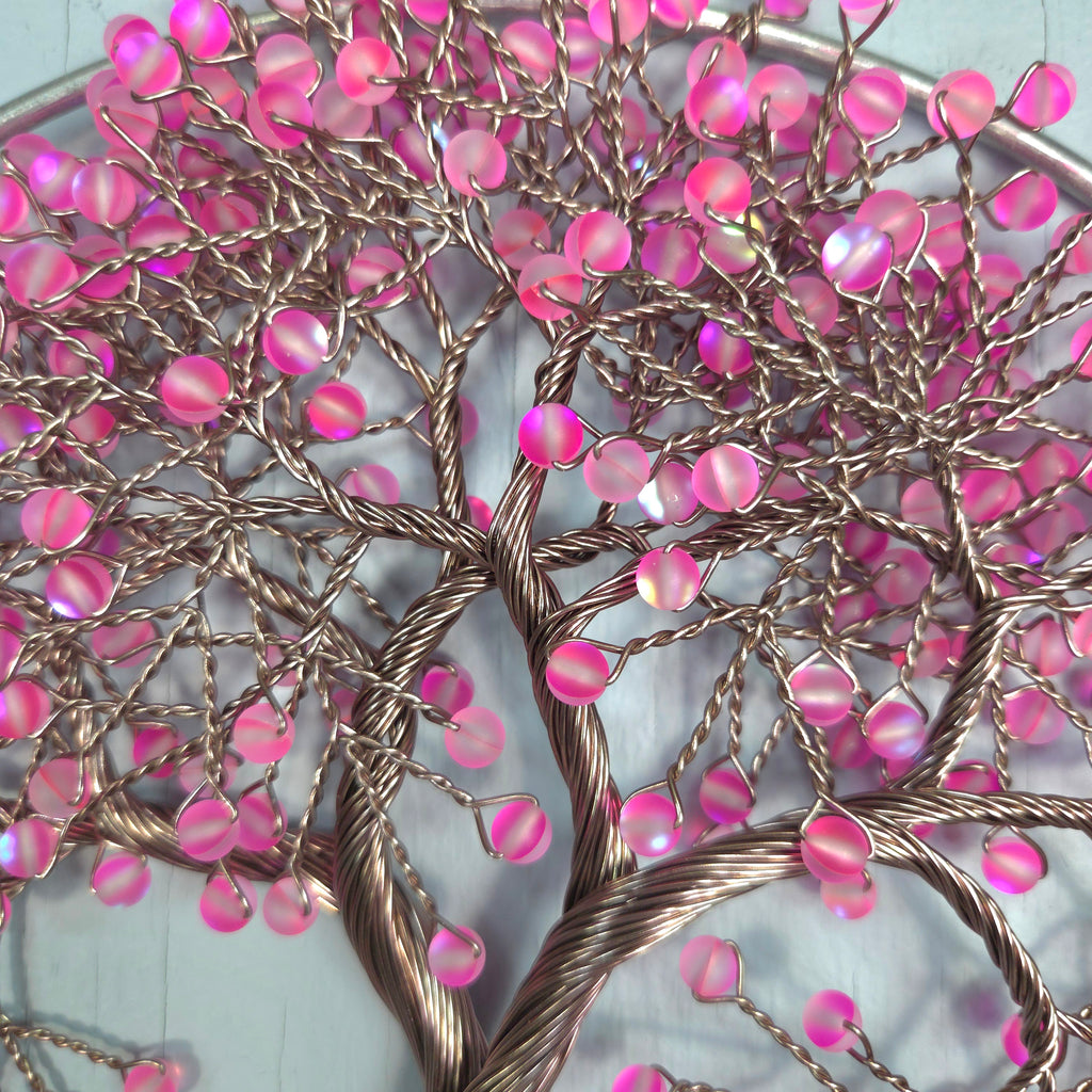 Decorative wall art with pink beads and braided wire on a white background