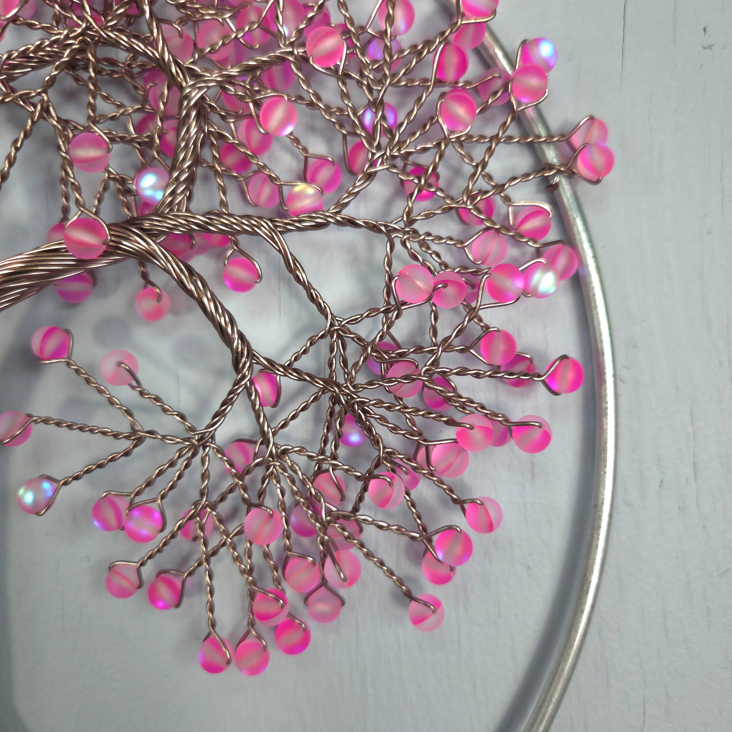 Decorative wall art with pink beads and metal branches on a light gray background