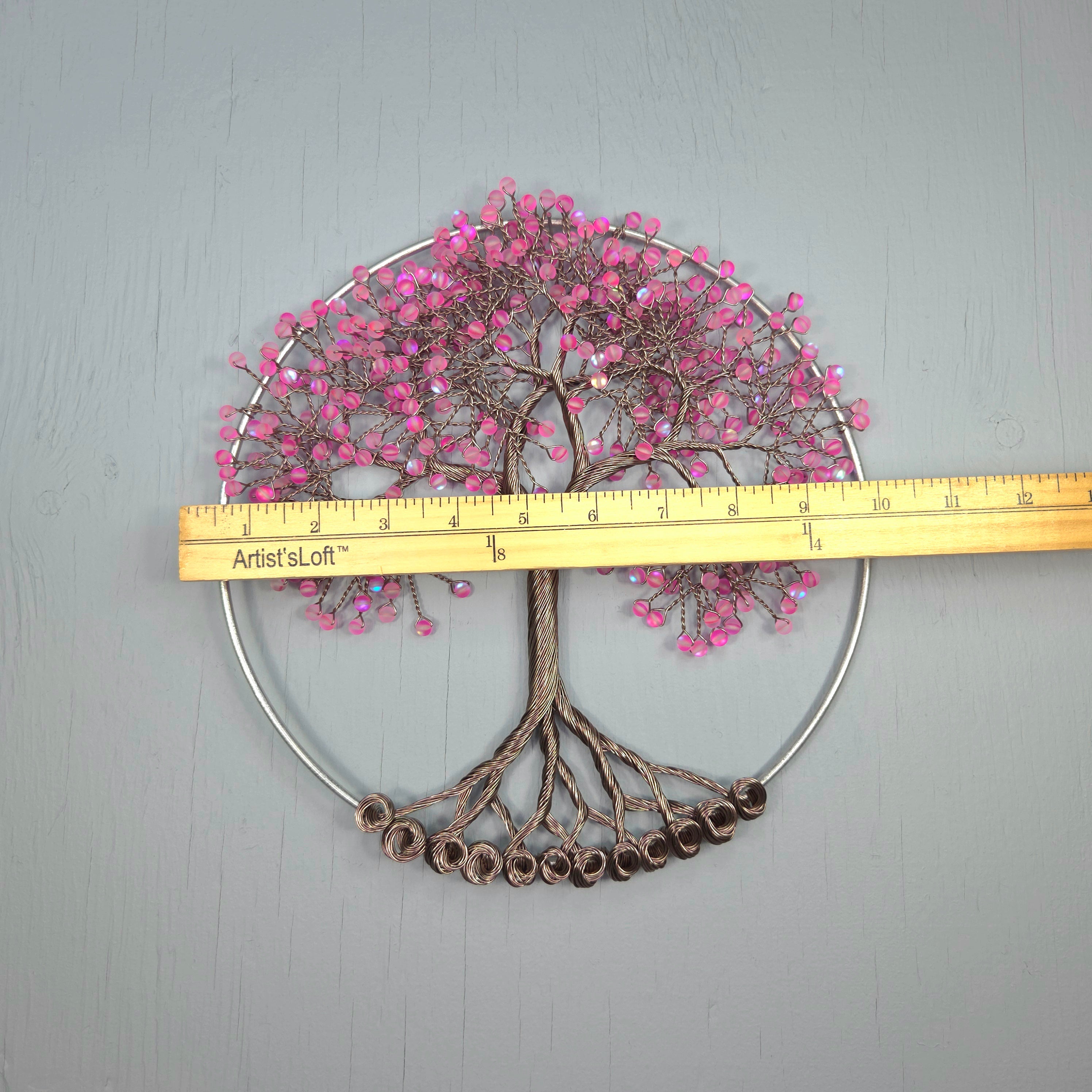 Decorative tree wall art with pink beads and a ruler for scale on a gray background