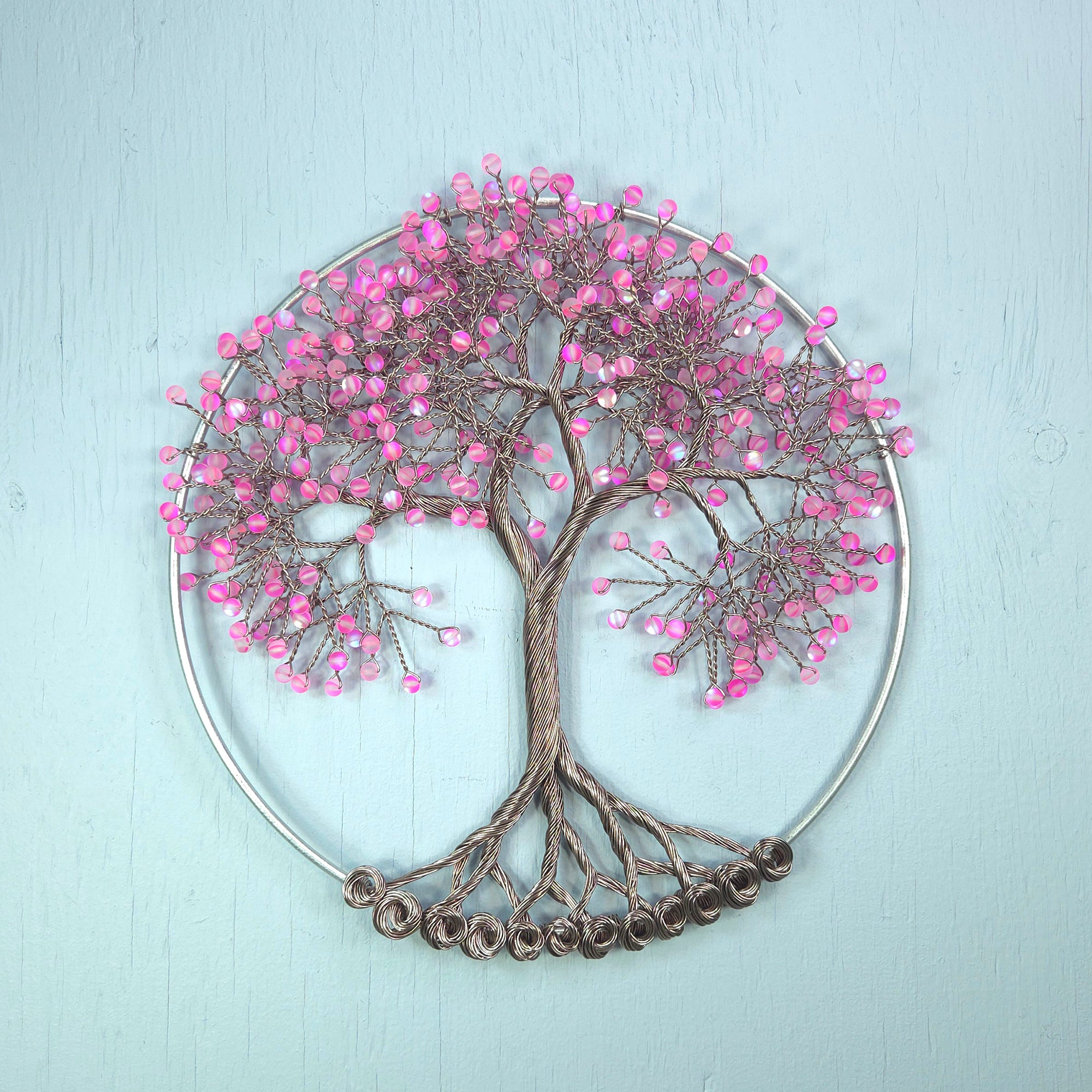 Decorative wall art in the shape of a tree with pink beads on a light blue background