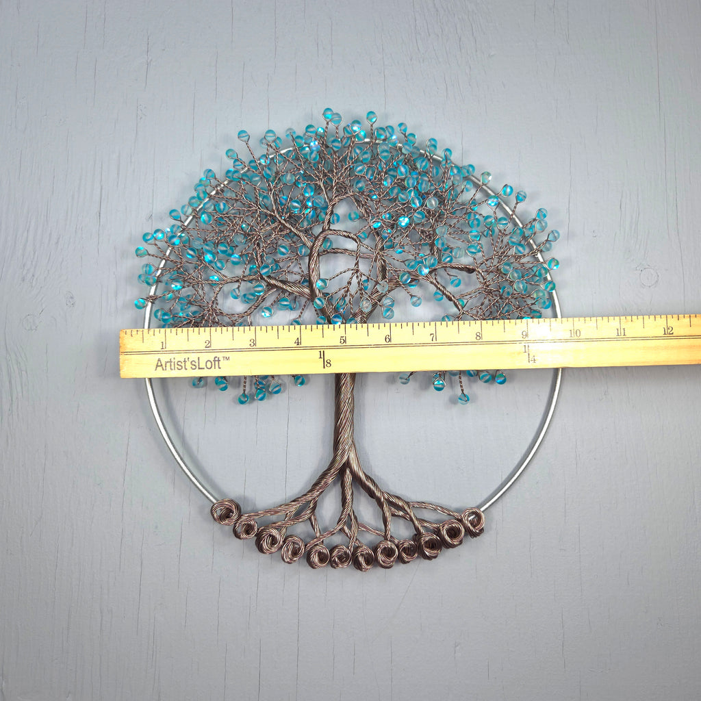 Decorative wall art of a tree with blue beads and metal base, measured against a ruler.