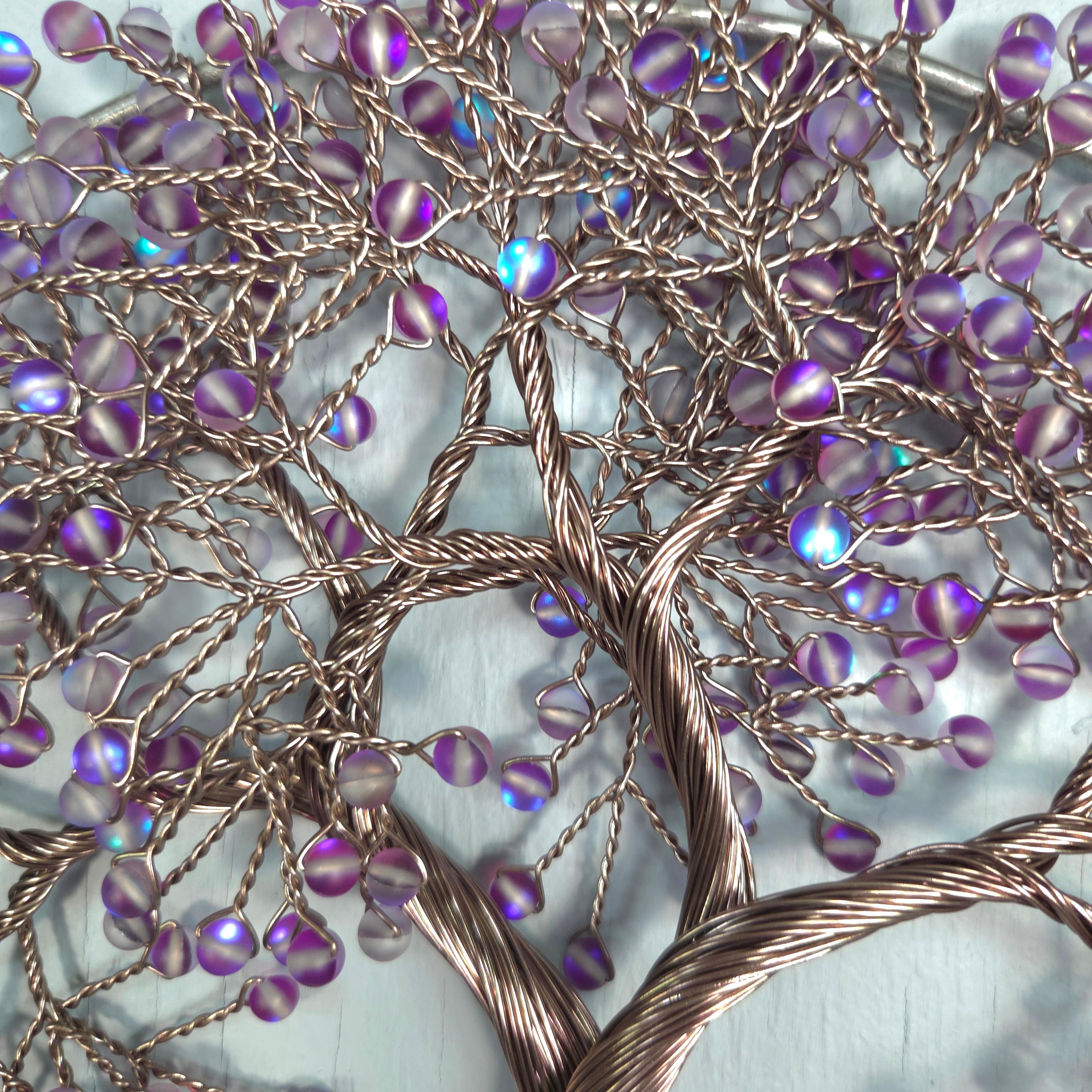 Decorative wall art with interwoven branches and purple beads on a textured background