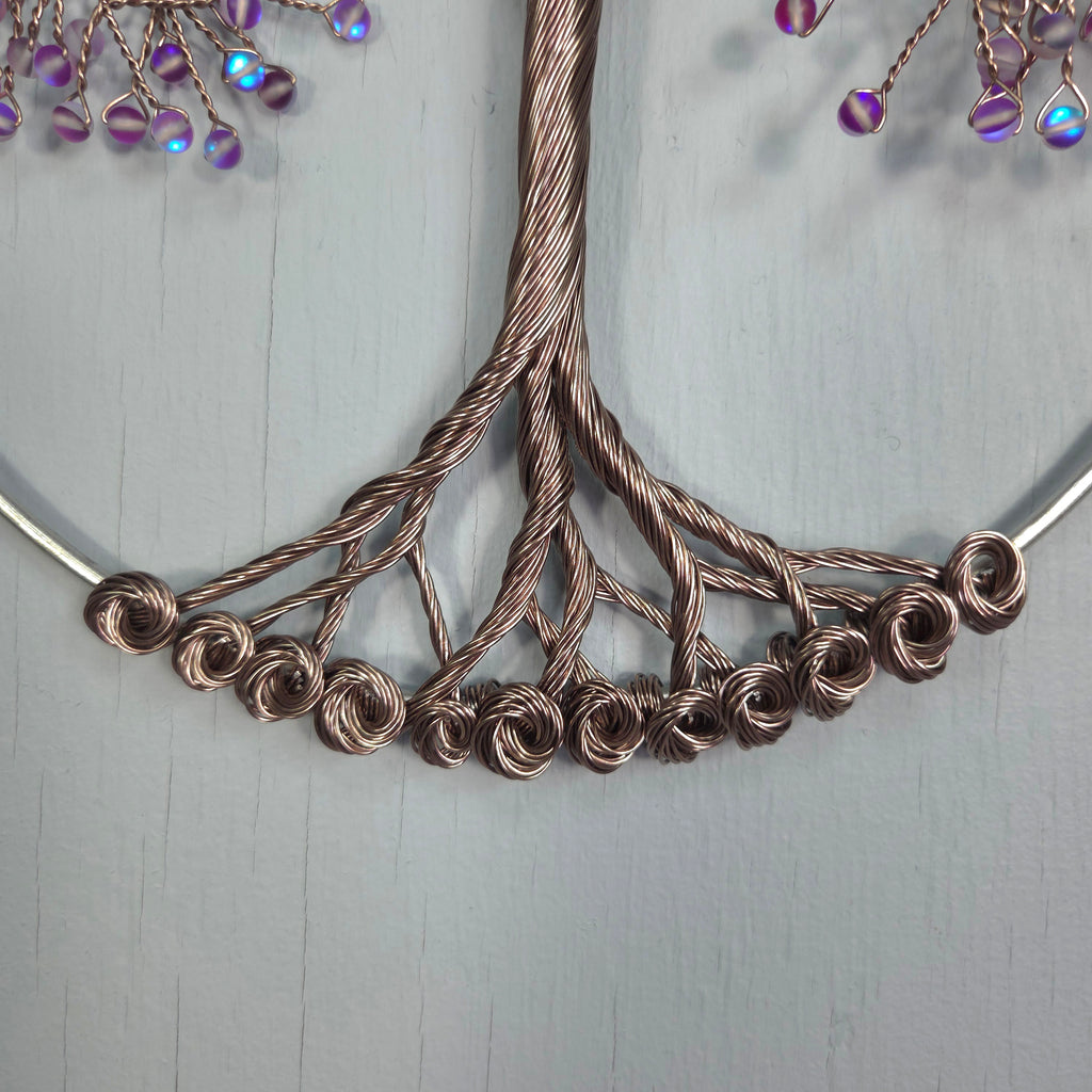 Close-up of a copper wire necklace with purple beads on a light gray background