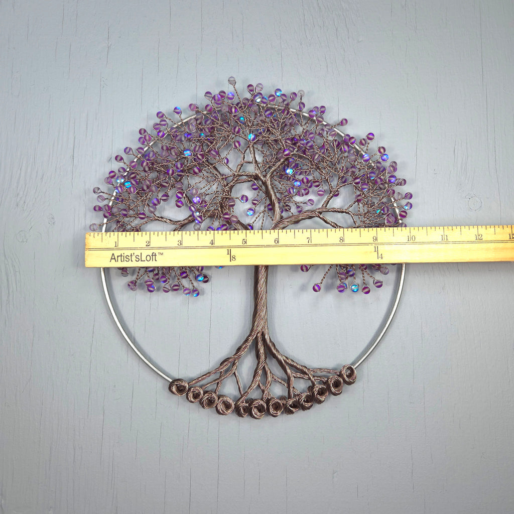 Decorative tree wall art with purple beads and a ruler for scale on a light gray background