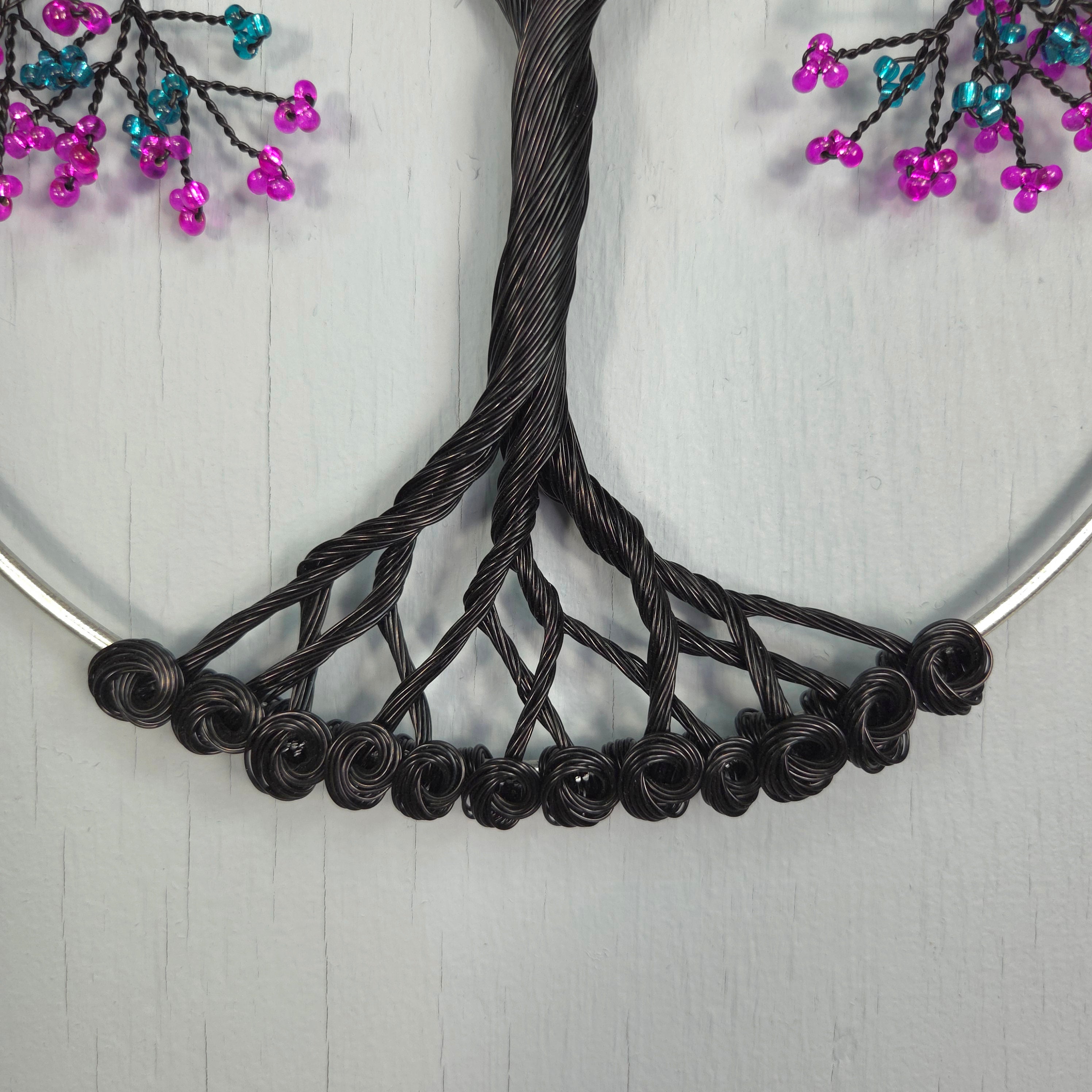 Black wire wreath with pink and blue beads on a white background