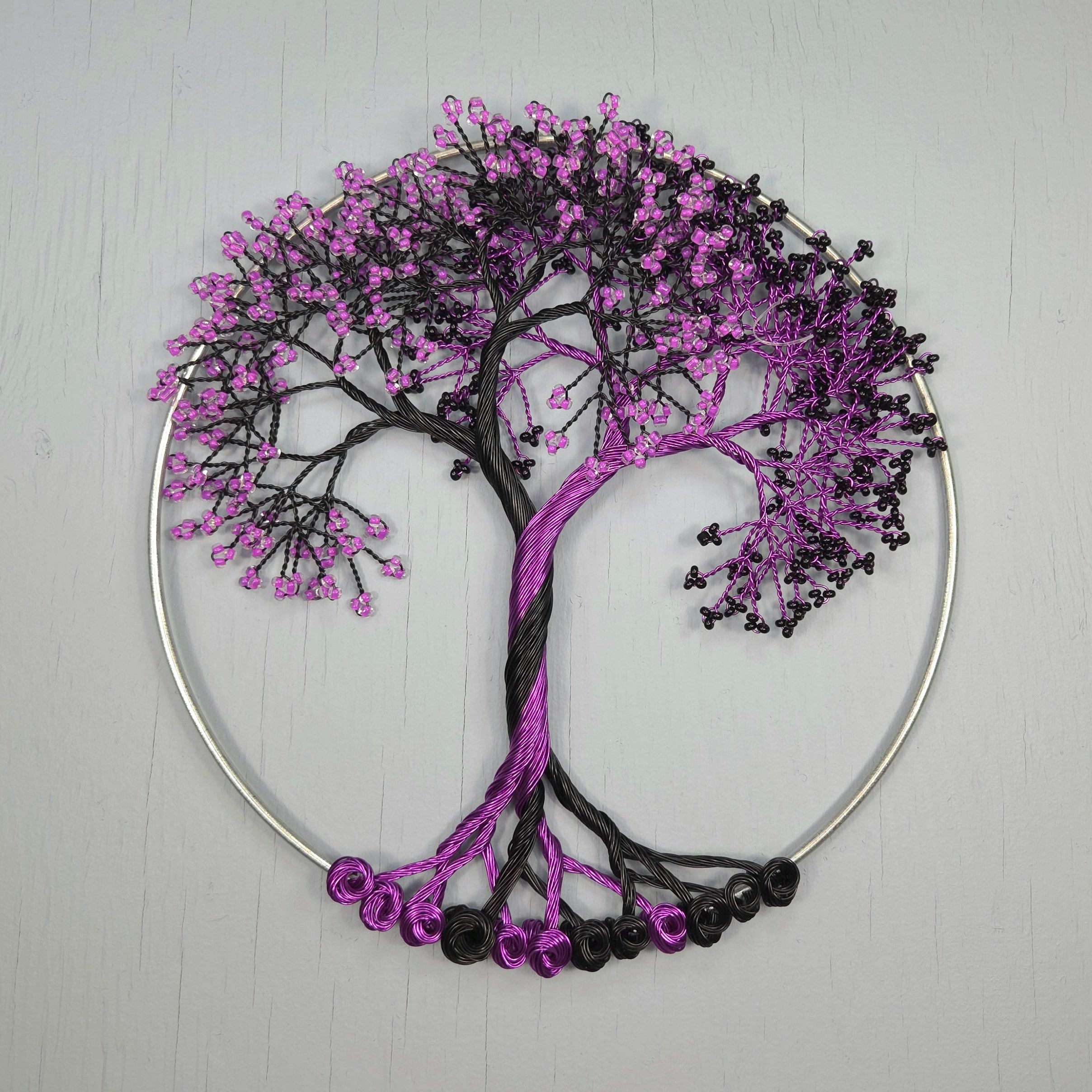 Decorative tree wall art with purple and black beads on a light gray background