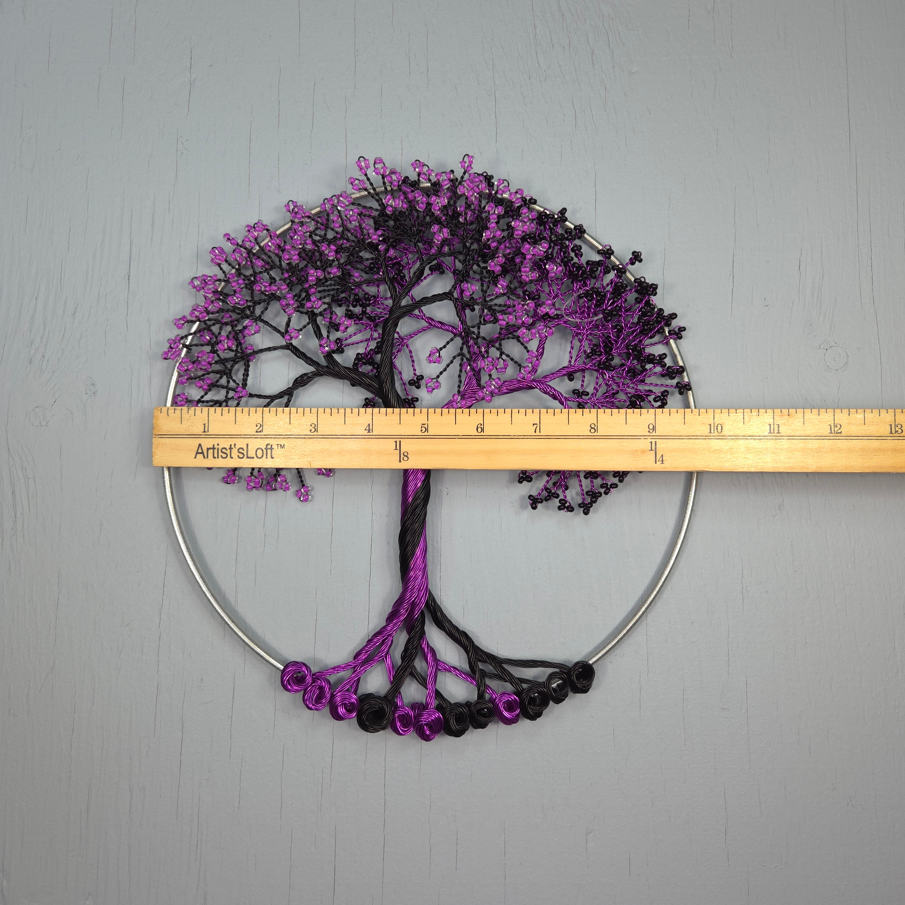 Decorative wall art with purple and black tree design next to a ruler on a gray background