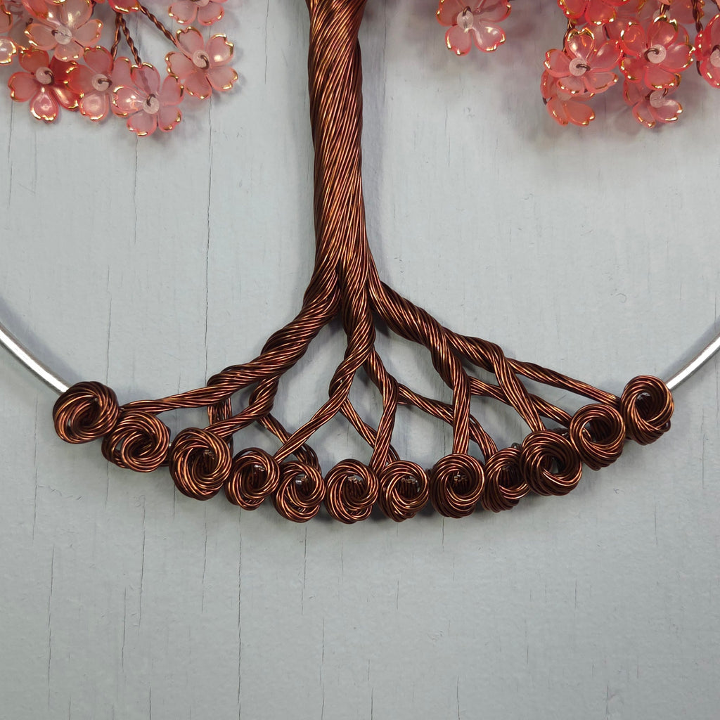 Necklace with copper wire design and pink floral elements on a light gray background