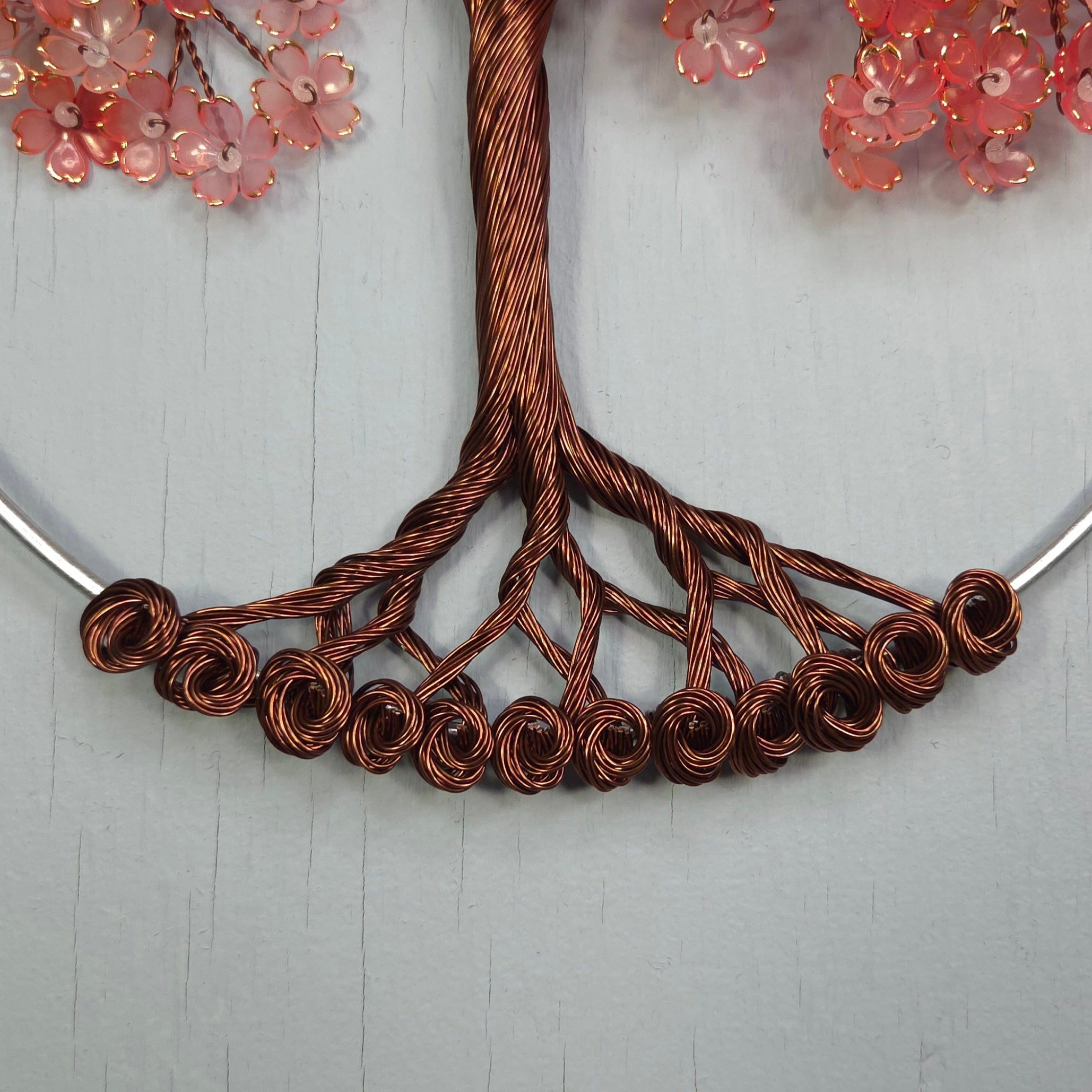 Necklace with copper wire design and pink floral elements on a light gray background