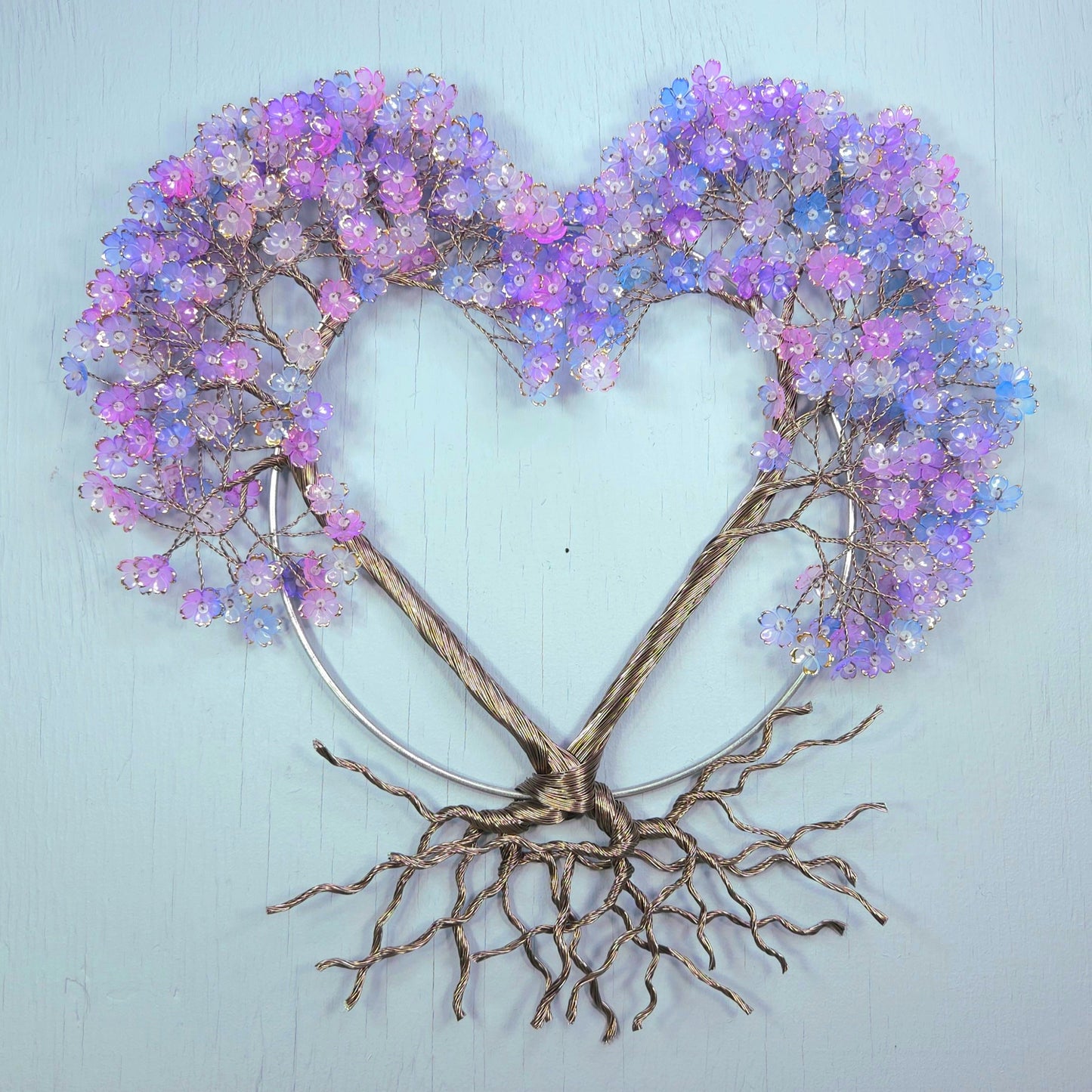 Decorative wall art with a heart shape made of branches and purple flowers on a light blue background.